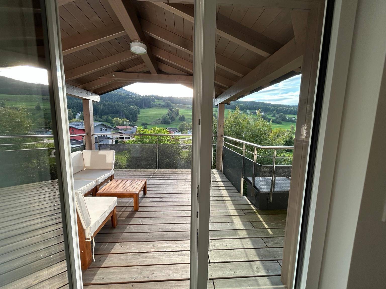 Blick durch die Glasschiebetür auf die überdachte Terrasse mit weitem Ausblick in die Natur.