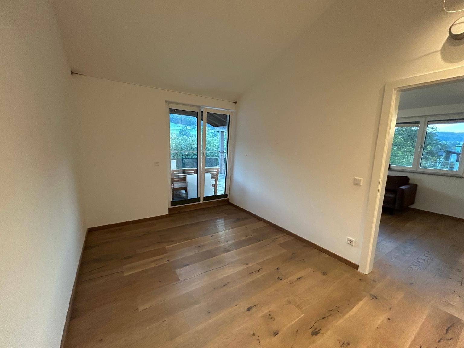 Leerer Raum mit Holzboden und Schiebetür, die zu einem Balkon oder einer Terrasse führt.