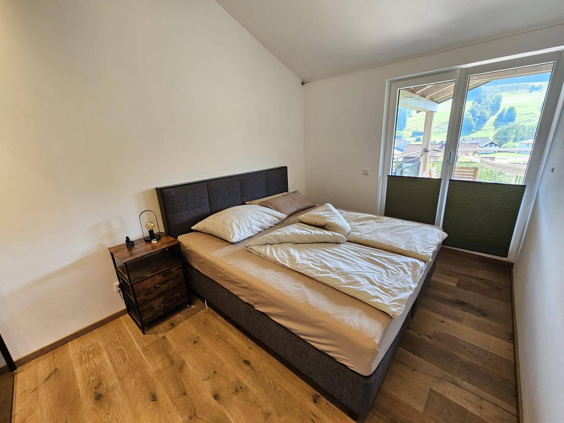 Schlafzimmer mit Doppelbett, Holzboden und Balkonzugang mit Bergblick.