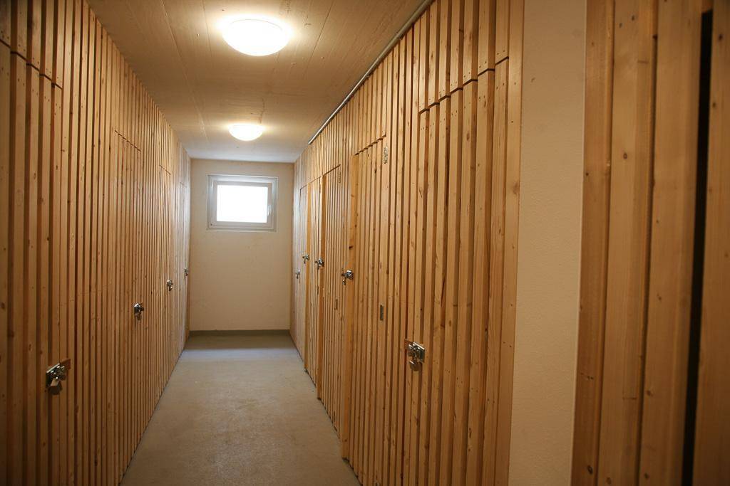 Langer Kellerflur mit zahlreichen Holzverschlägen für zusätzlichen Stauraum und einem kleinen Fenster.
