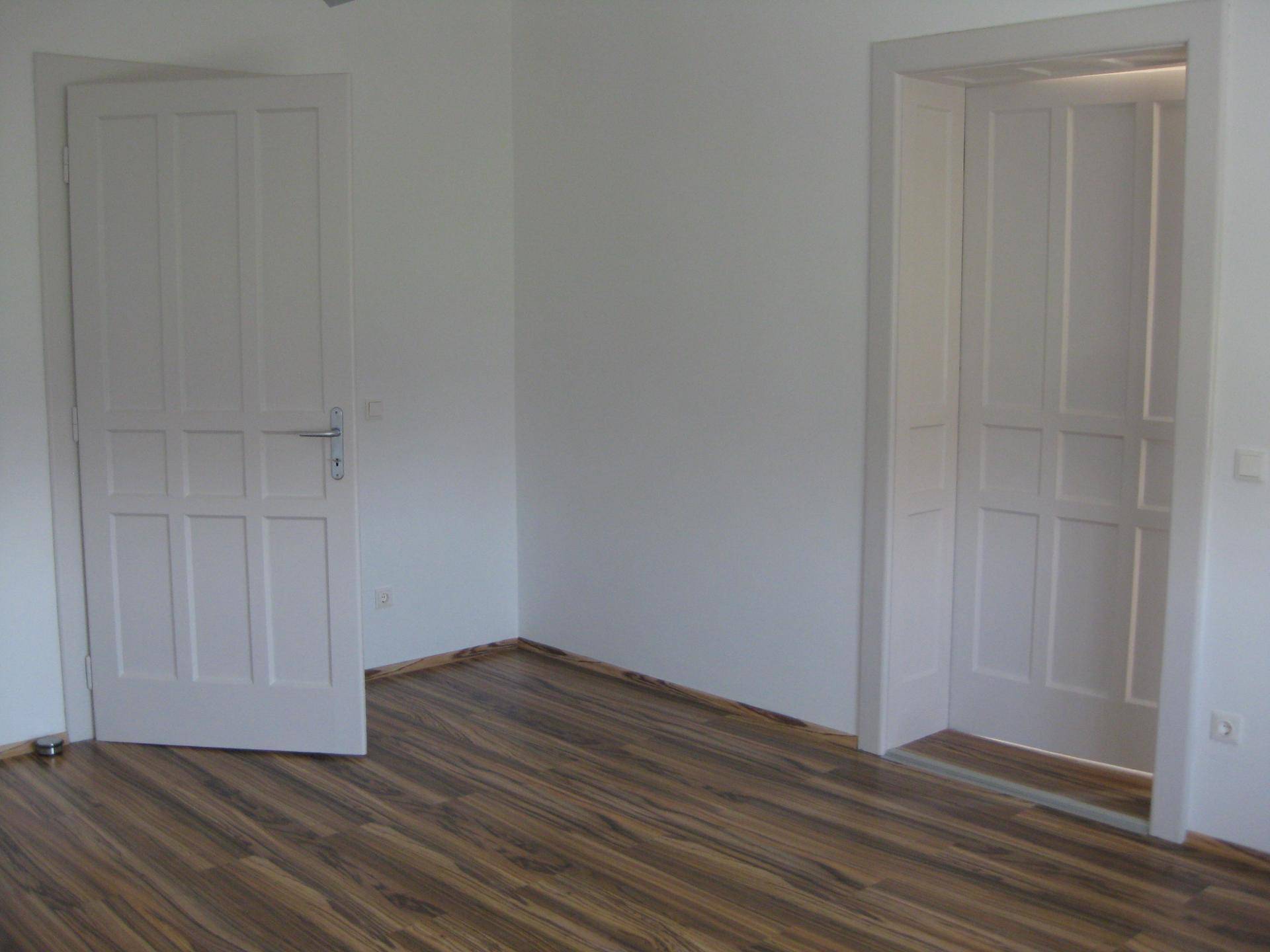 Leerer Raum mit zwei weißen Türen und einem Holzlaminatboden, der auf die Einrichtung wartet.
