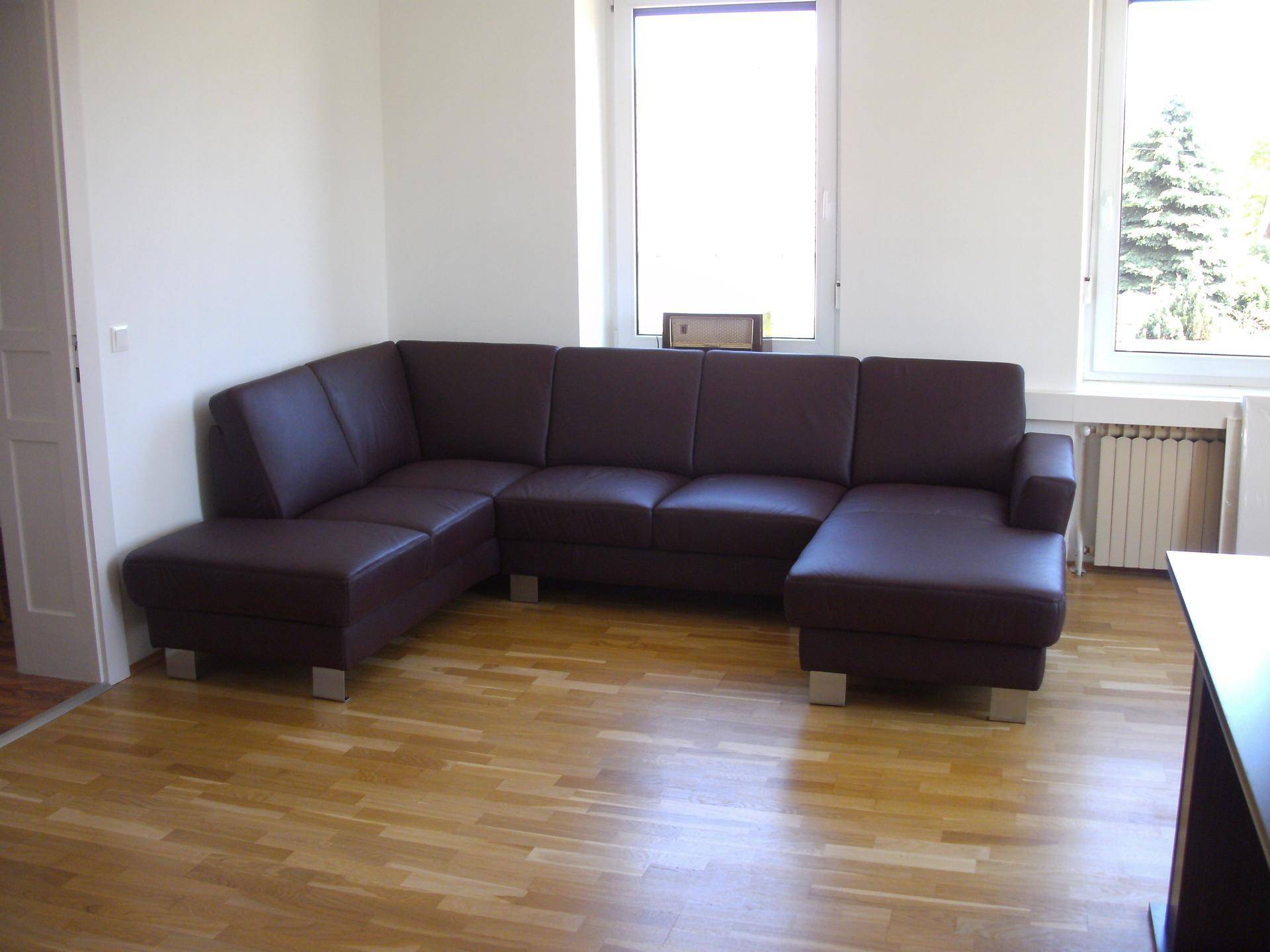 Gemütlicher Wartebereich mit einer großen braunen Ledercouch und hellem Holzfußboden vor einem Fenster.