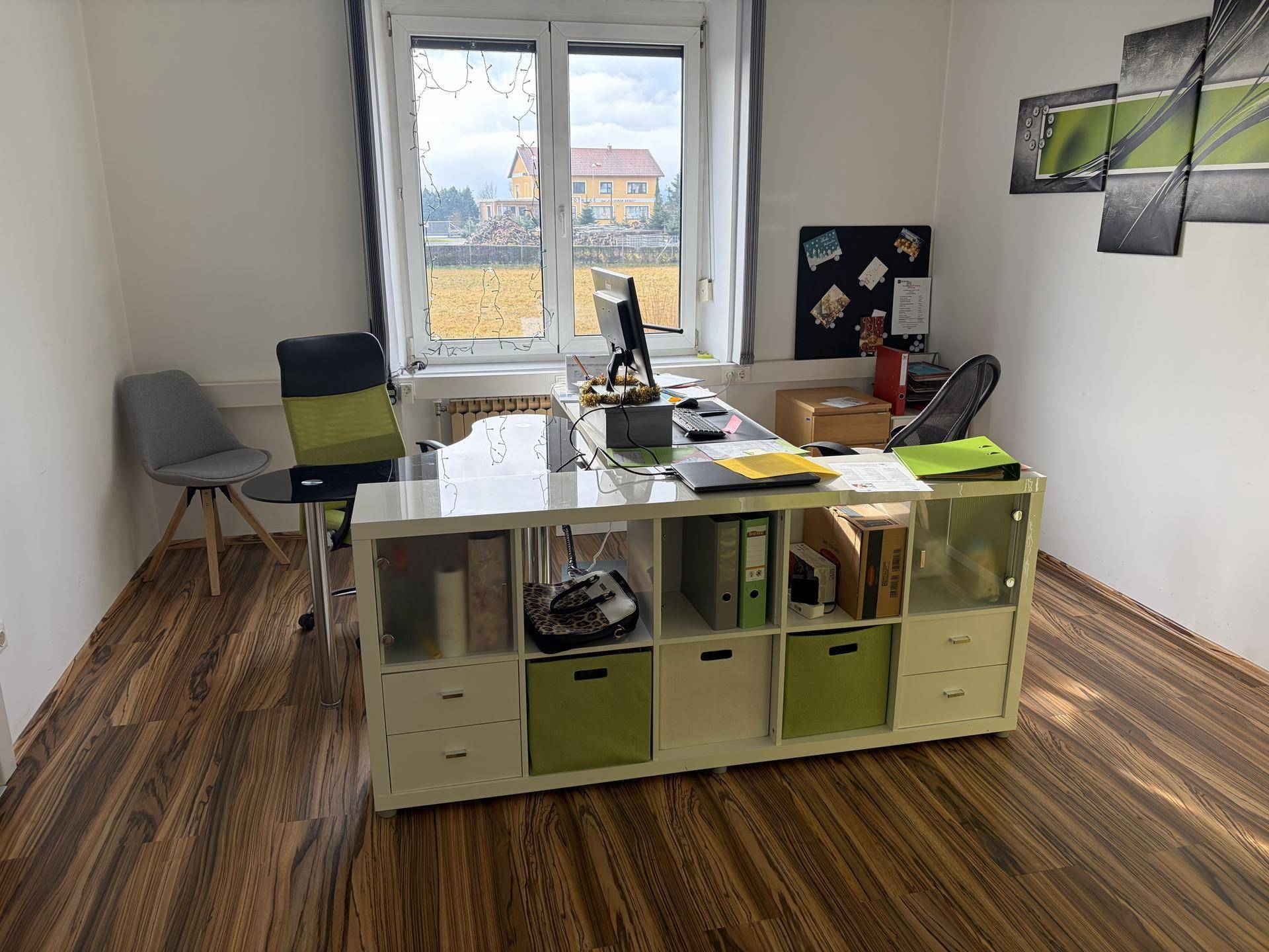 Helles Büro mit großem Fenster, Schreibtisch und einem Regalsystem mit grünen Akzenten.