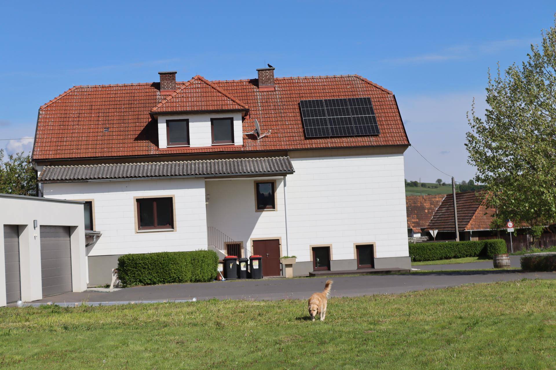 Weißes Wohnhaus mit rotem Ziegeldach, Solarpaneelen und einer Garage, umgeben von einer grünen Wiese.