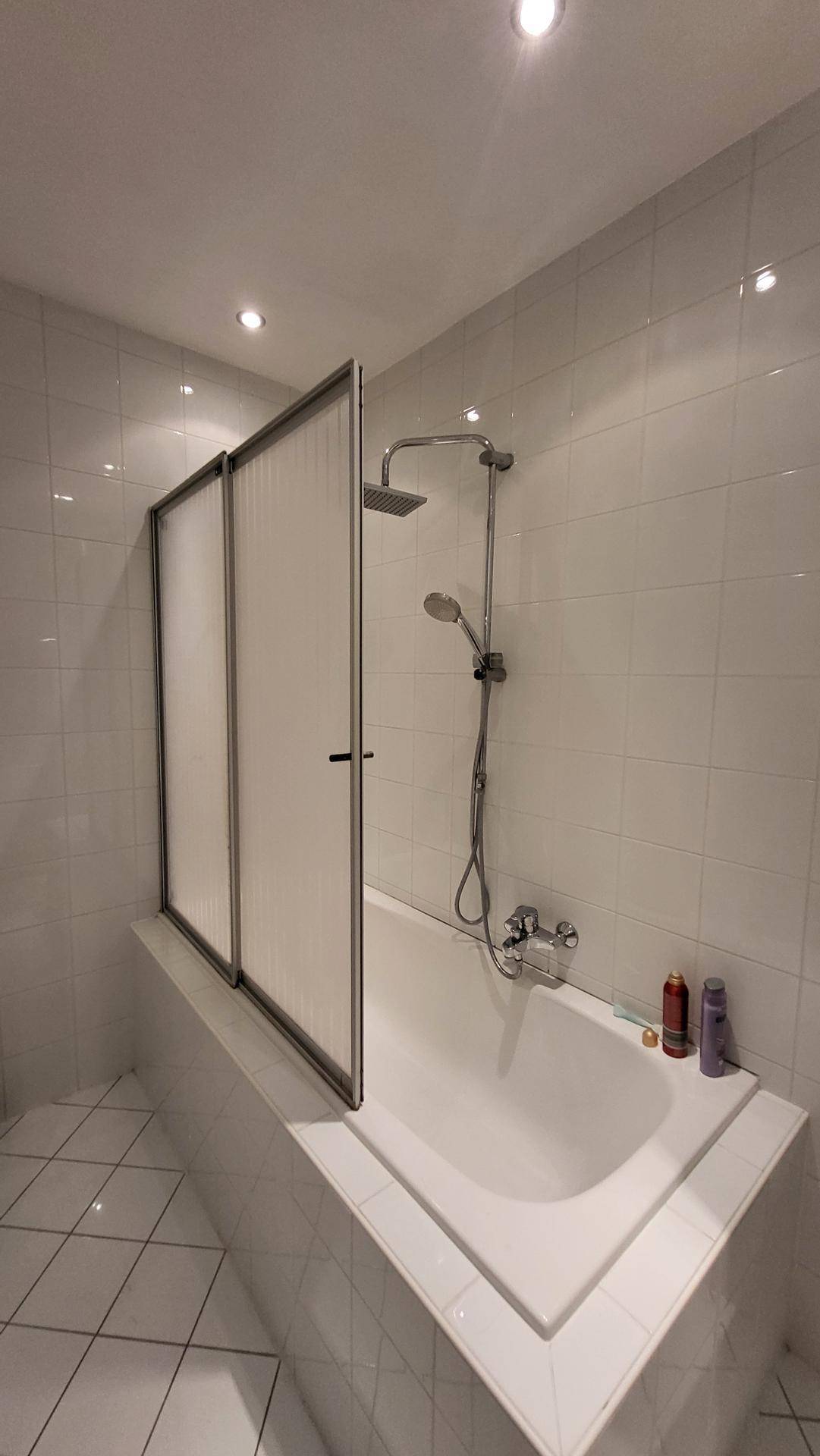 Badezimmer mit Badewanne, Duschabtrennung und Fliesenboden.
