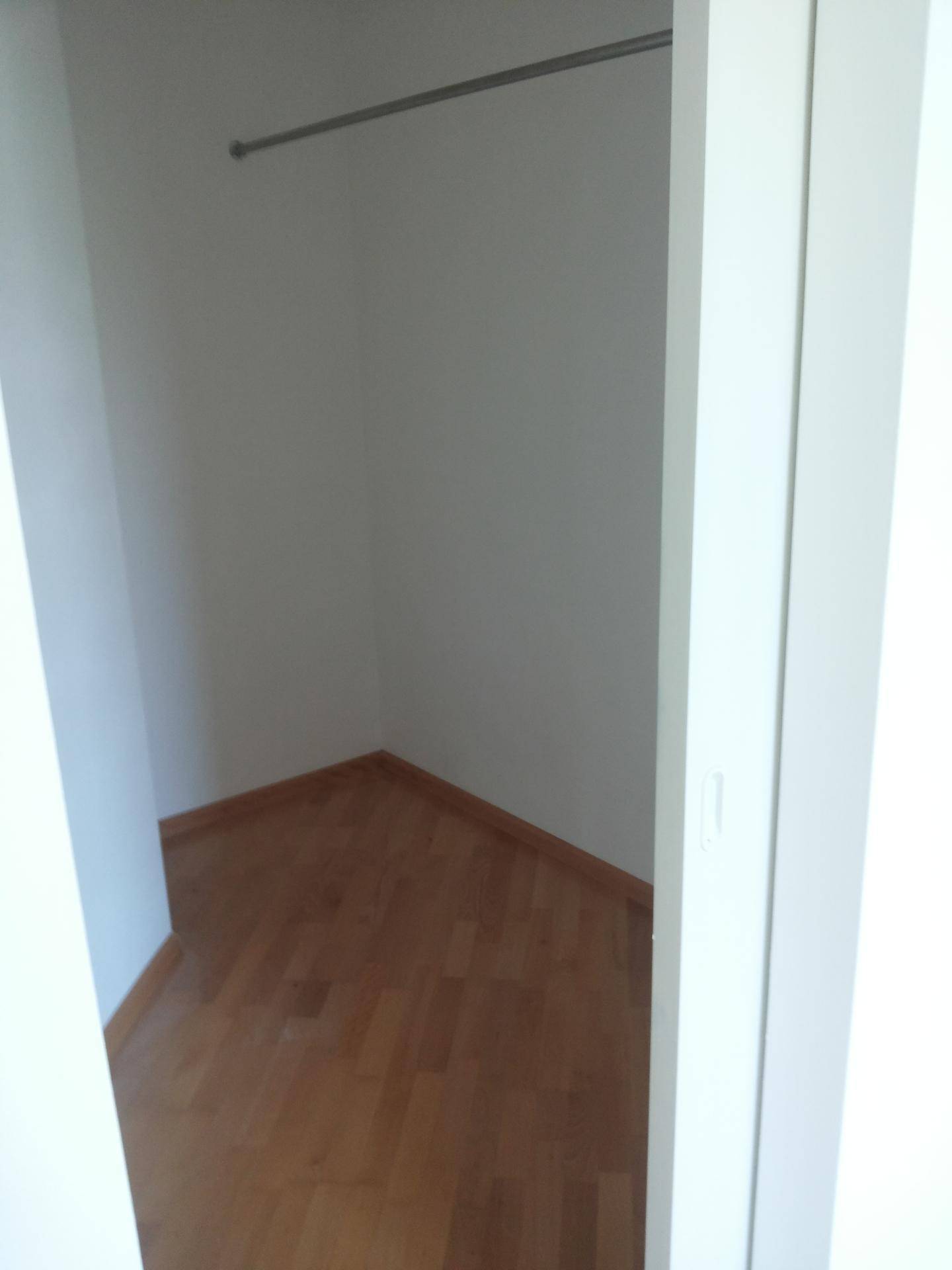 Praktischer begehbarer Kleiderschrank mit Kleiderstange und Parkettboden.