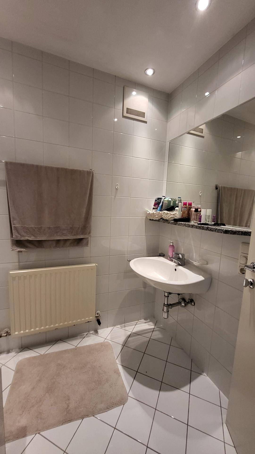 Modernes Badezimmer mit Waschbecken, Spiegel und Heizkörper, hell gefliest.