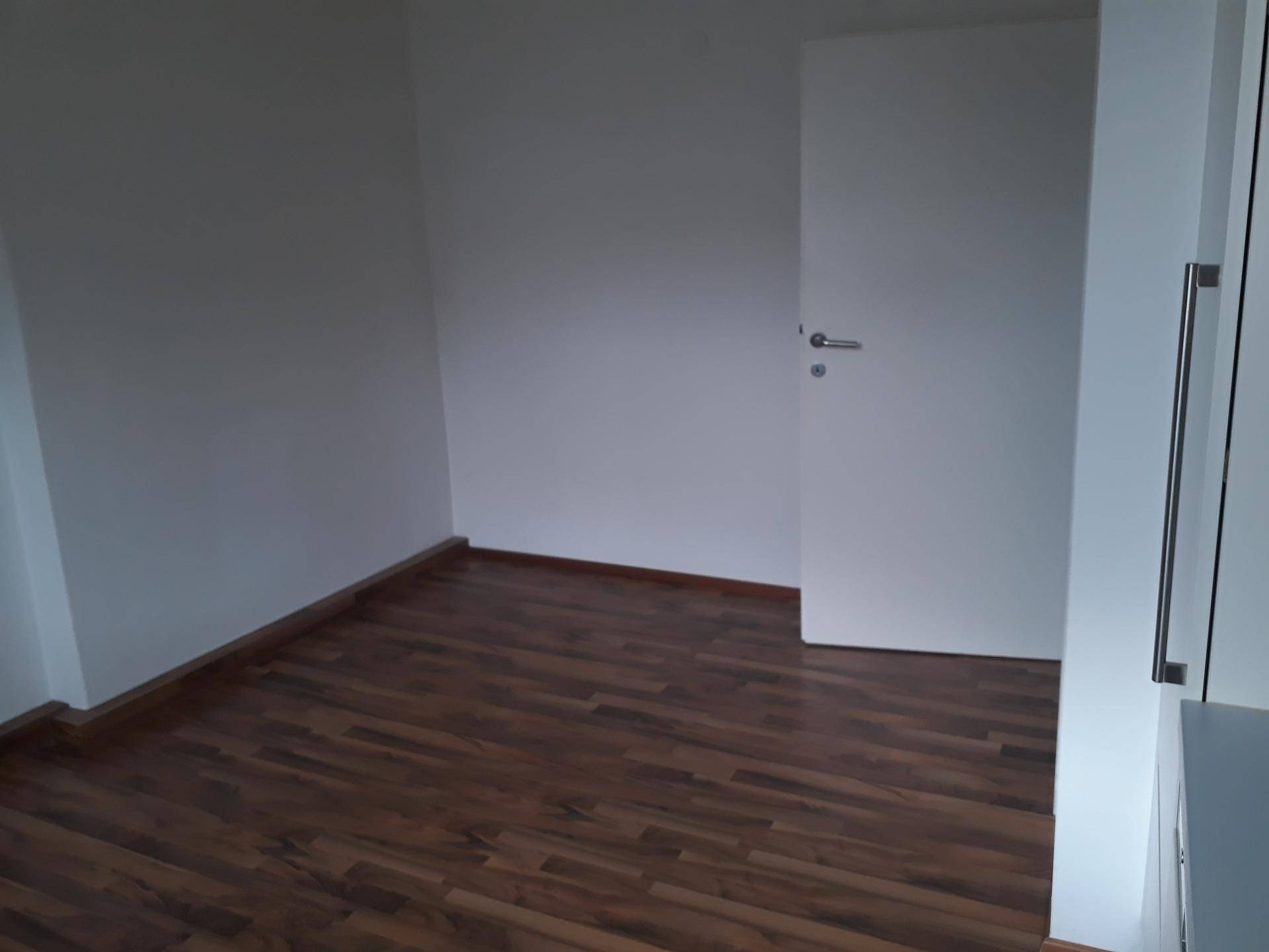 Leerer Raum mit Laminatboden und weißen Wänden, bereit zur individuellen Gestaltung.