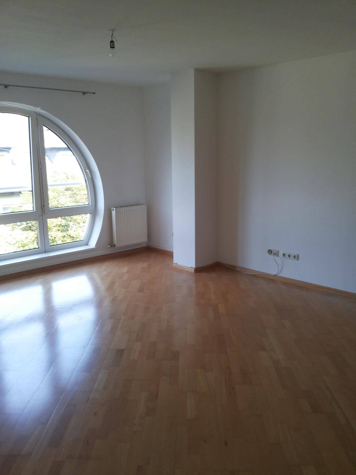 Leerer Raum mit hellem Parkettboden und markanten Rundbogenfenstern.
