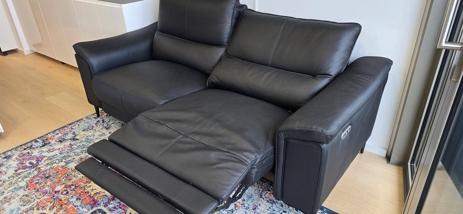 Bequemes schwarzes Ledersofa mit verstellbarer Fußstütze auf einem farbenfrohen Teppich.