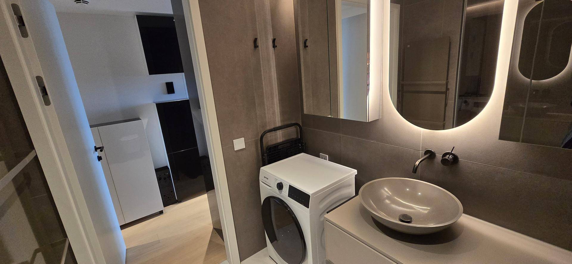 Stilvolles Badezimmer mit modernem Design, Aufsatzwaschbecken und integrierter Waschmaschine.