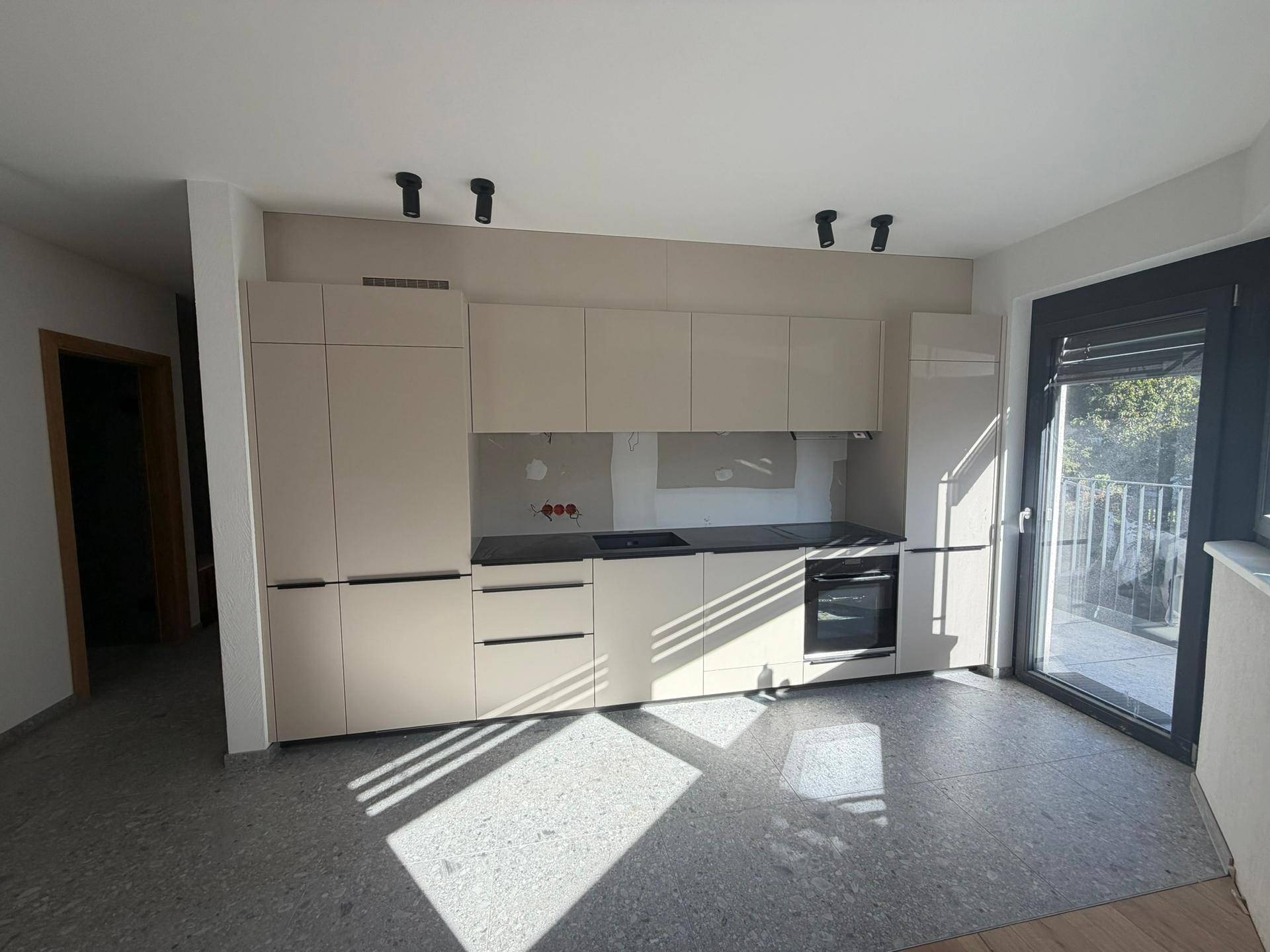 Moderne Küche mit beigen Schränken, integriertem Backofen und Balkonzugang.