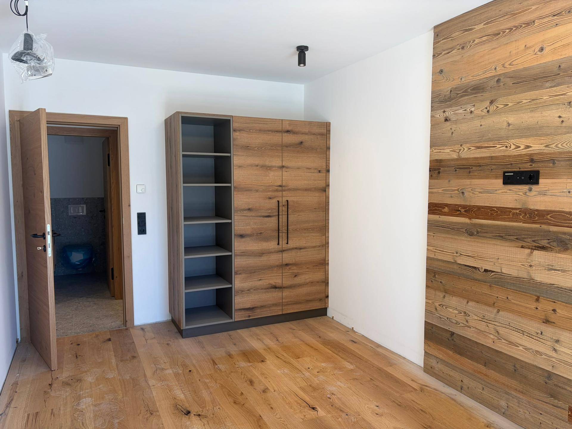 Schlafzimmer mit Holzboden, Einbauschrank und einer markanten Holzwand, die einen rustikalen Charme verleiht.