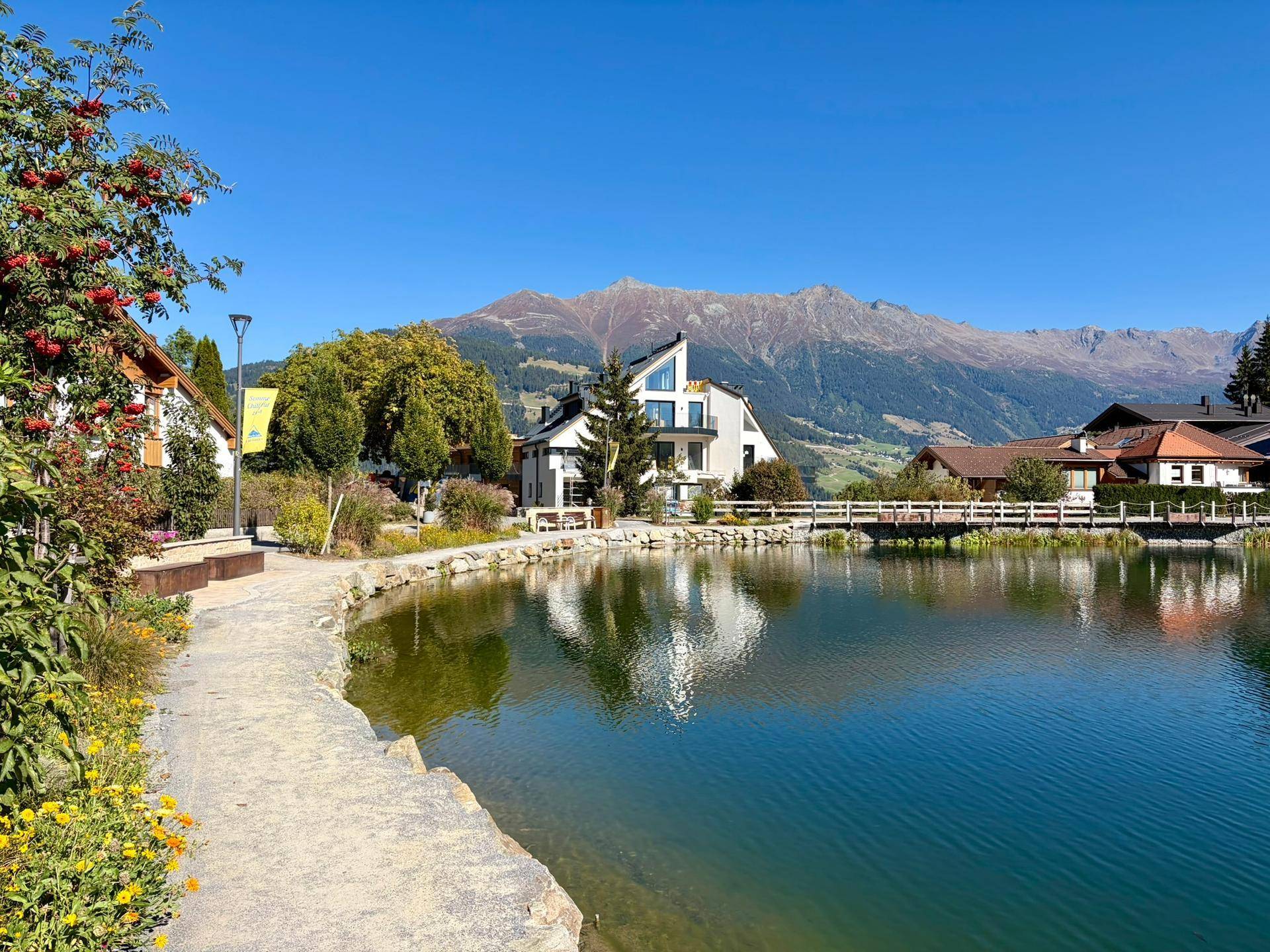 Panoramablick auf den See mit umliegenden Häusern, üppiger Vegetation und einer beeindruckenden Bergkulisse.