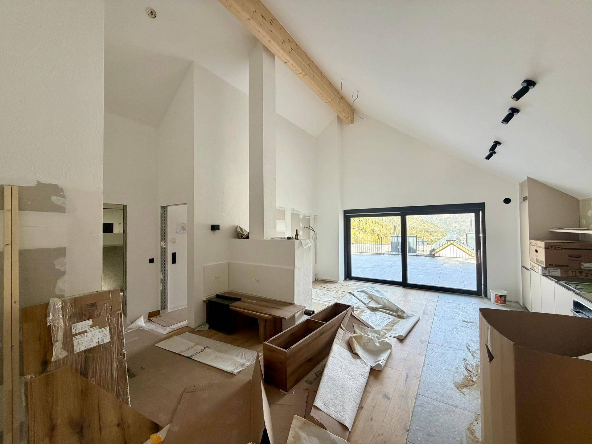 Heller Wohnbereich im Rohbau mit hohen Gewölbedecken, sichtbaren Holzbalken und Terrassenzugang.