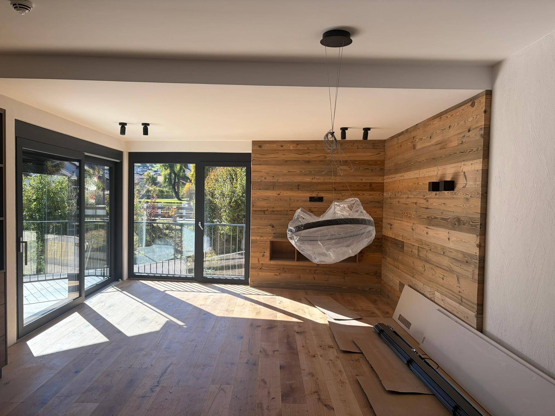 Helles Wohnzimmer im Rohbau mit Holzwandverkleidung und großen Fenstern, die viel Licht hereinlassen.