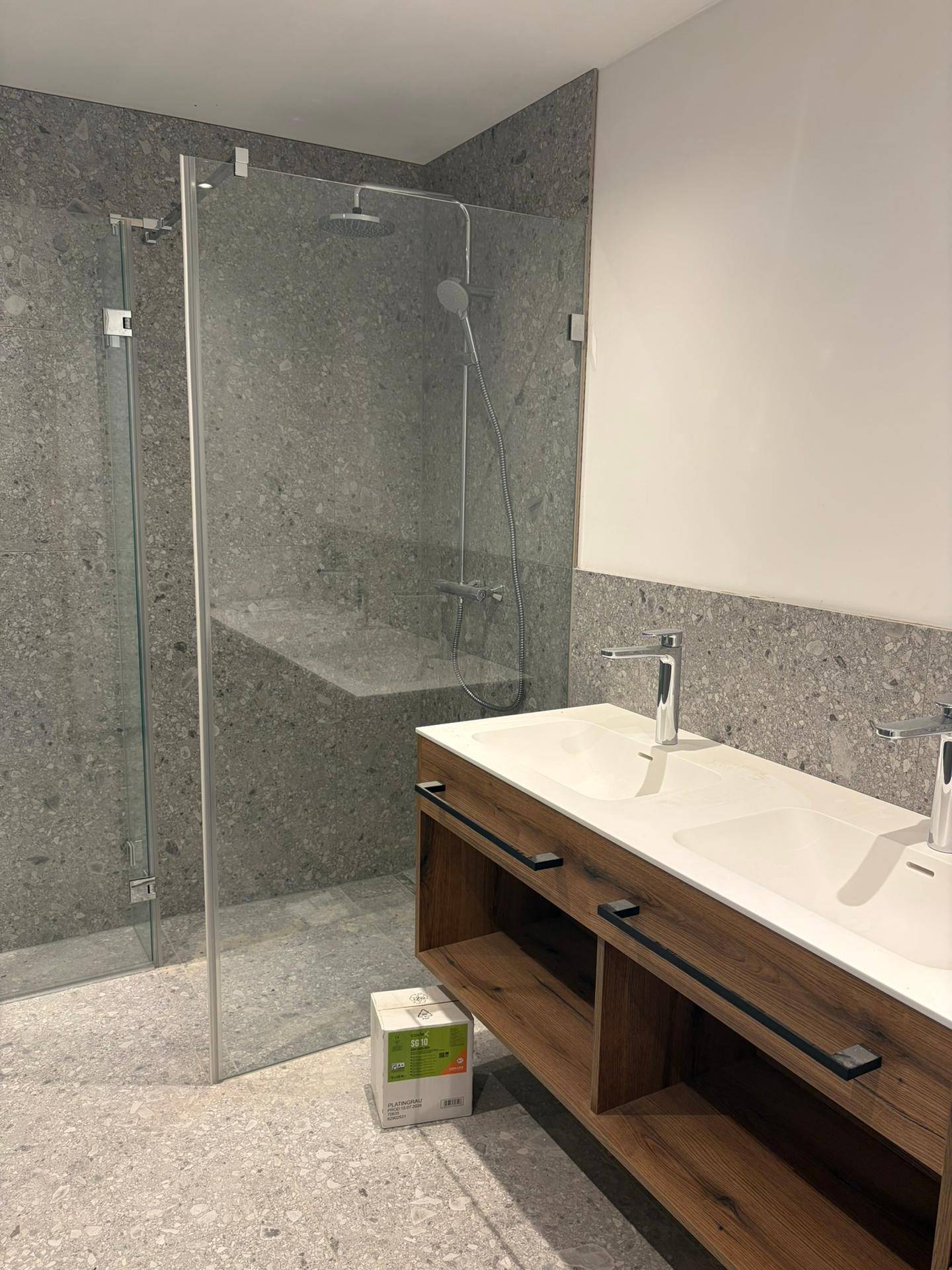Modernes Badezimmer mit doppelten Waschbecken, begehbarer Dusche und grauen Fliesen.