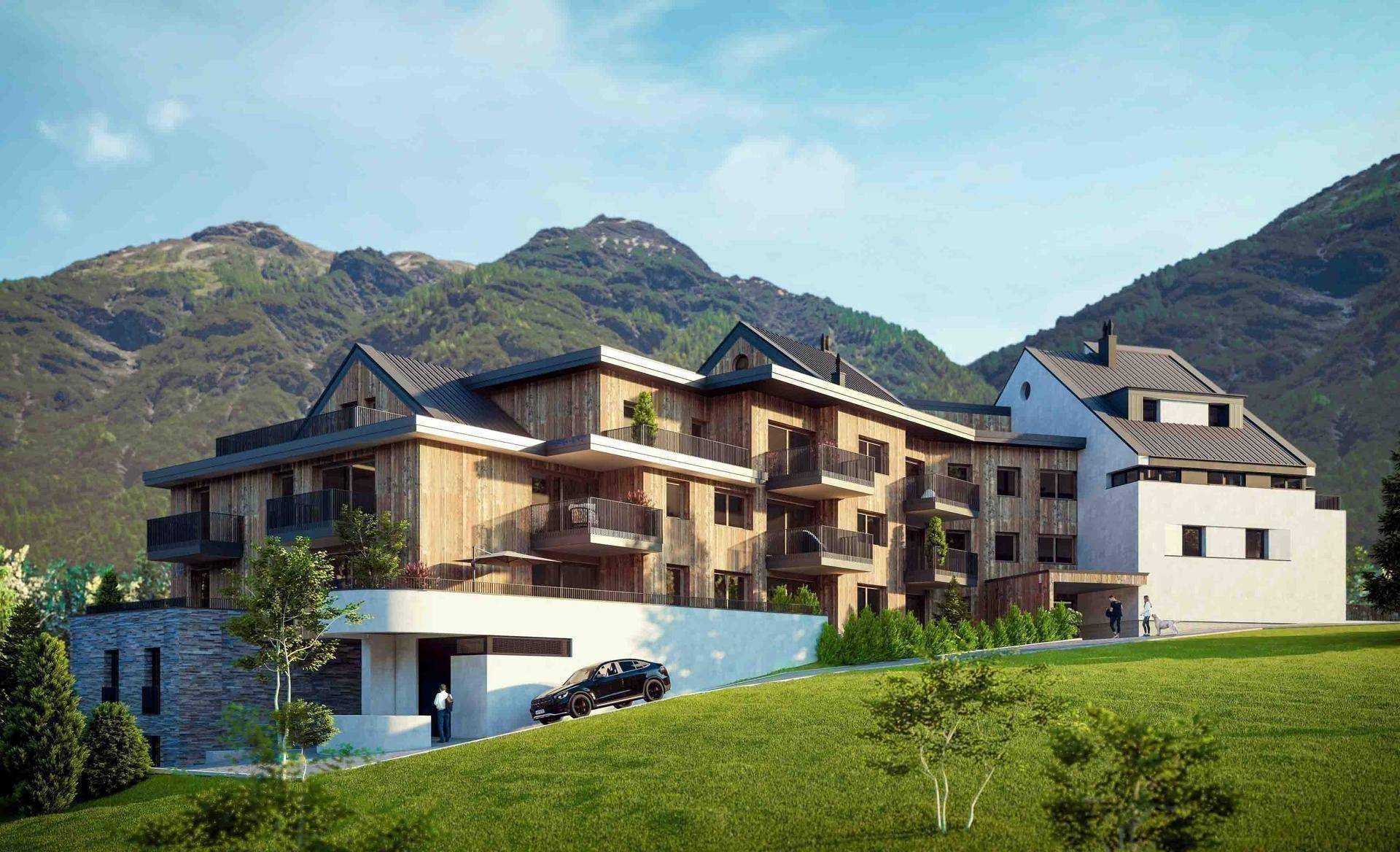 Modernes Gebäude mit Holz- und Steinfassade, Balkonen und einer Auffahrt in alpiner Umgebung.