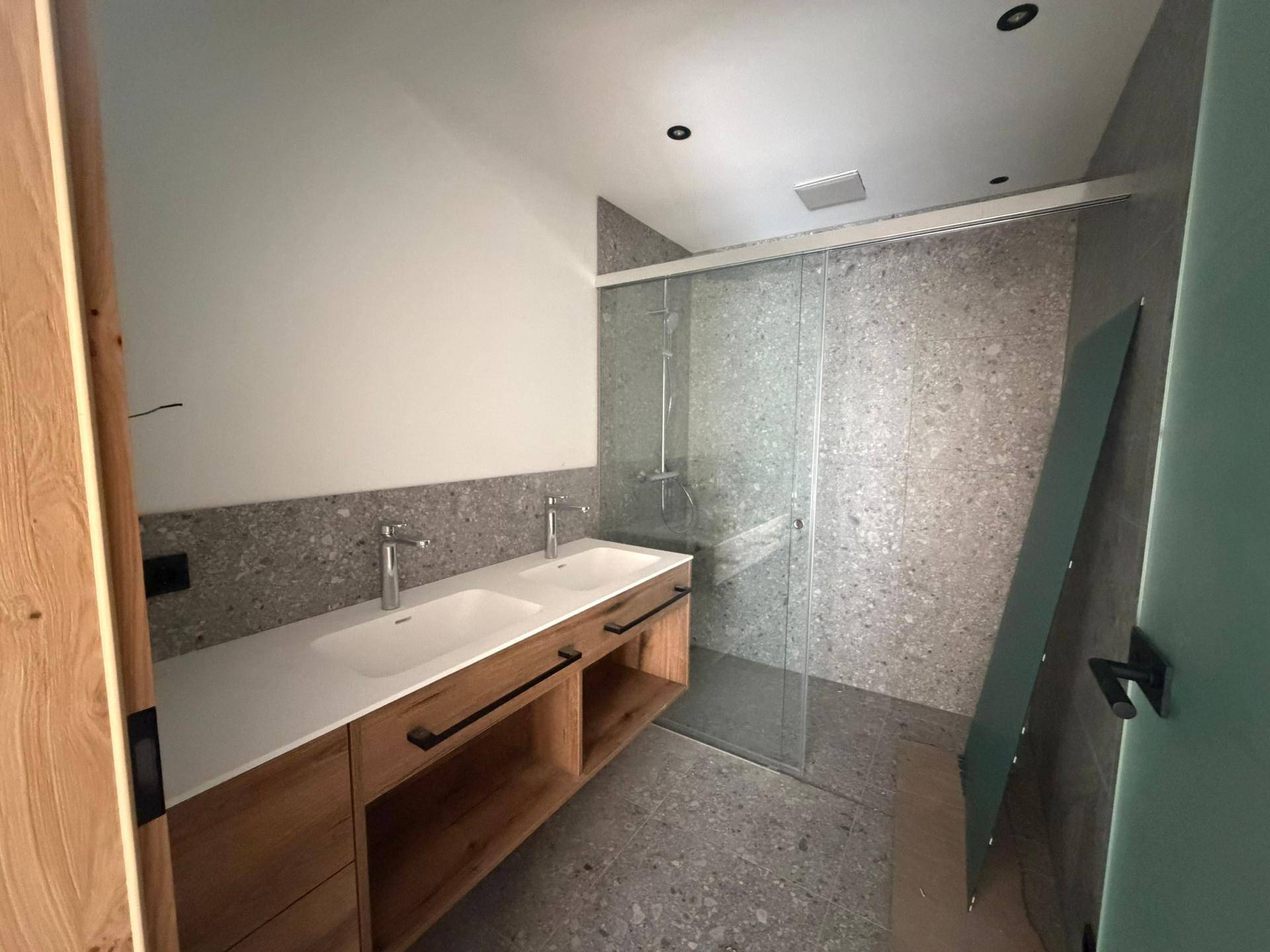 Modernes Badezimmer mit Doppelwaschbecken, großer Dusche und grauen Fliesen.