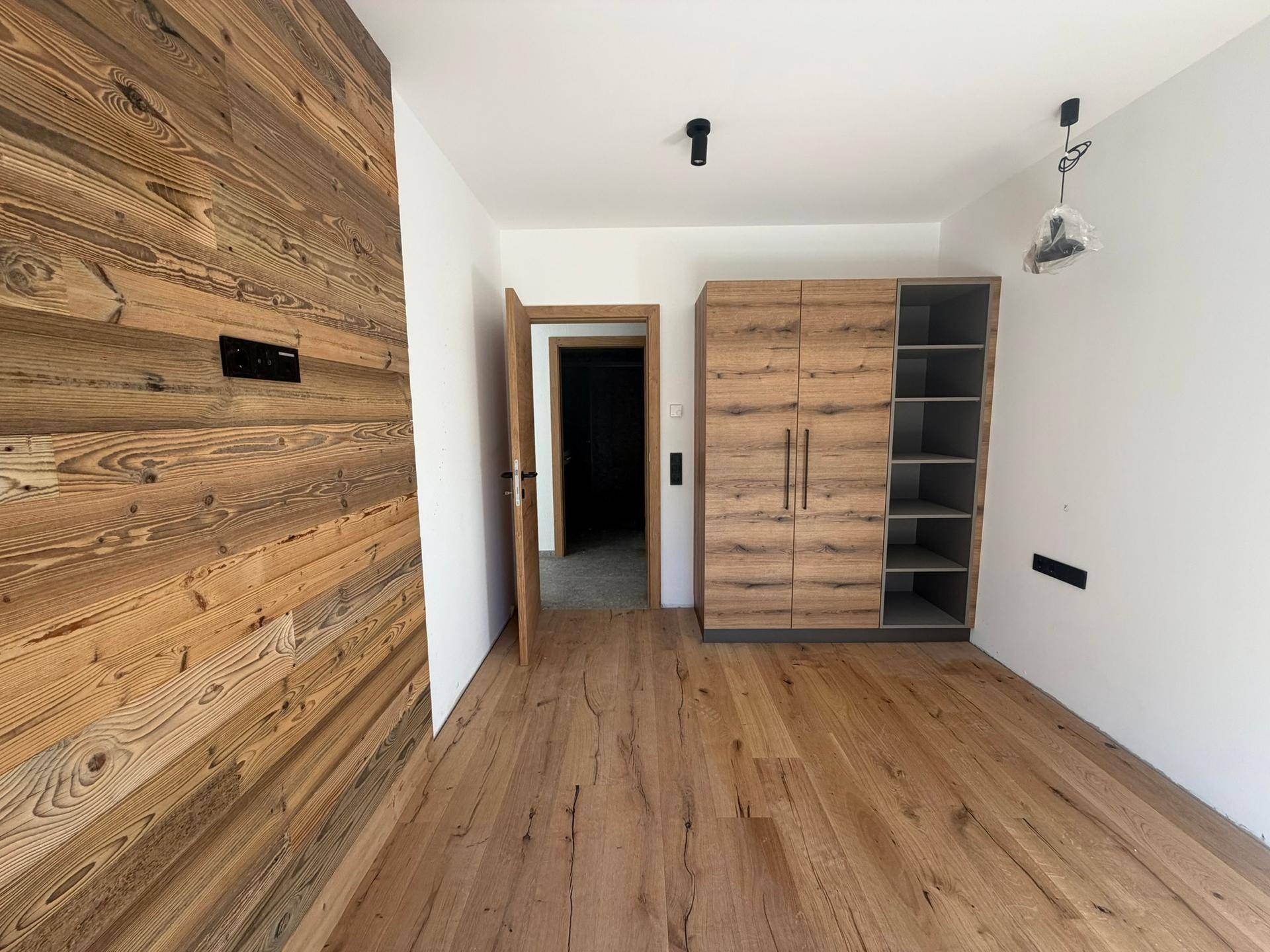 Schlafzimmer mit Holzwänden, Holzboden und einem modernen Kleiderschrank.