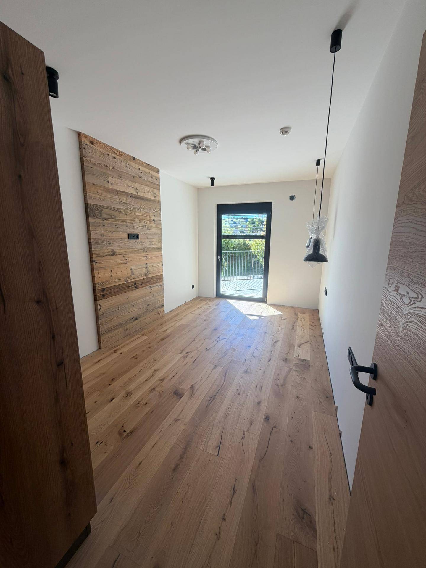Helles Schlafzimmer mit Holzwandakzent, Parkettboden und Zugang zu einem französischen Balkon.