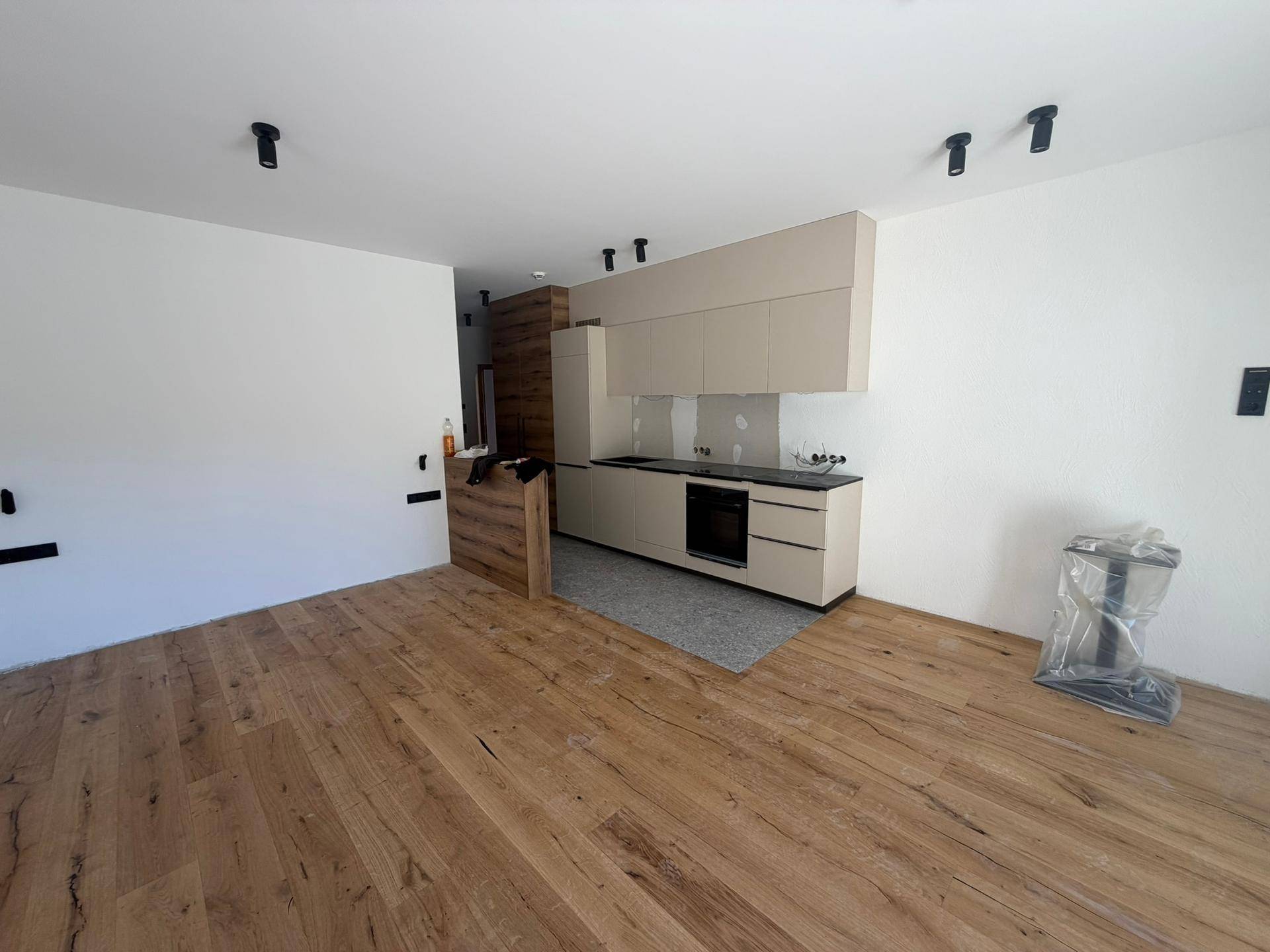 Moderne Einbauküche in Beige mit dunklen Arbeitsplatten, integrierten Geräten und Holzfußboden.