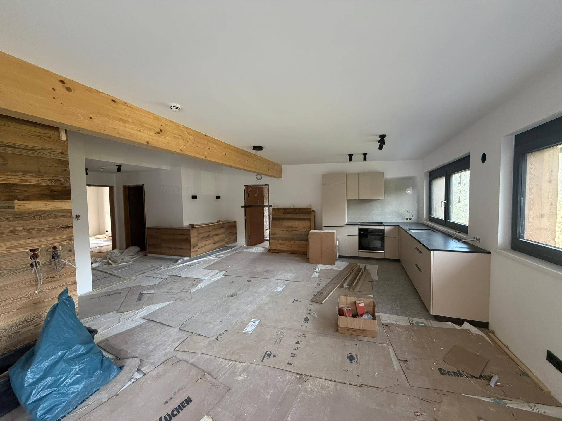 Offener Wohnbereich im Bau mit Holzwänden, sichtbarem Holzbalken und moderner Küchenzeile.