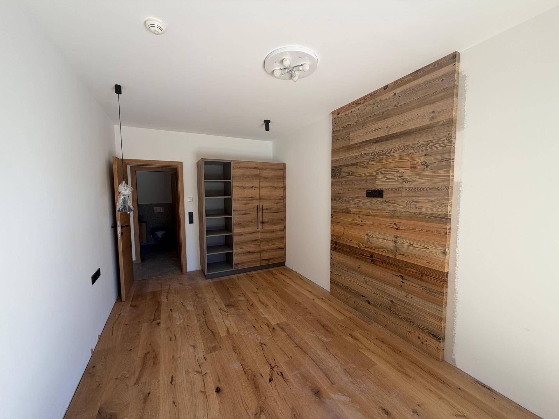 Schlafzimmer im Rohbau mit Holzwandakzent und hochwertigem Holzfußboden, der eine warme Atmosphäre schafft.