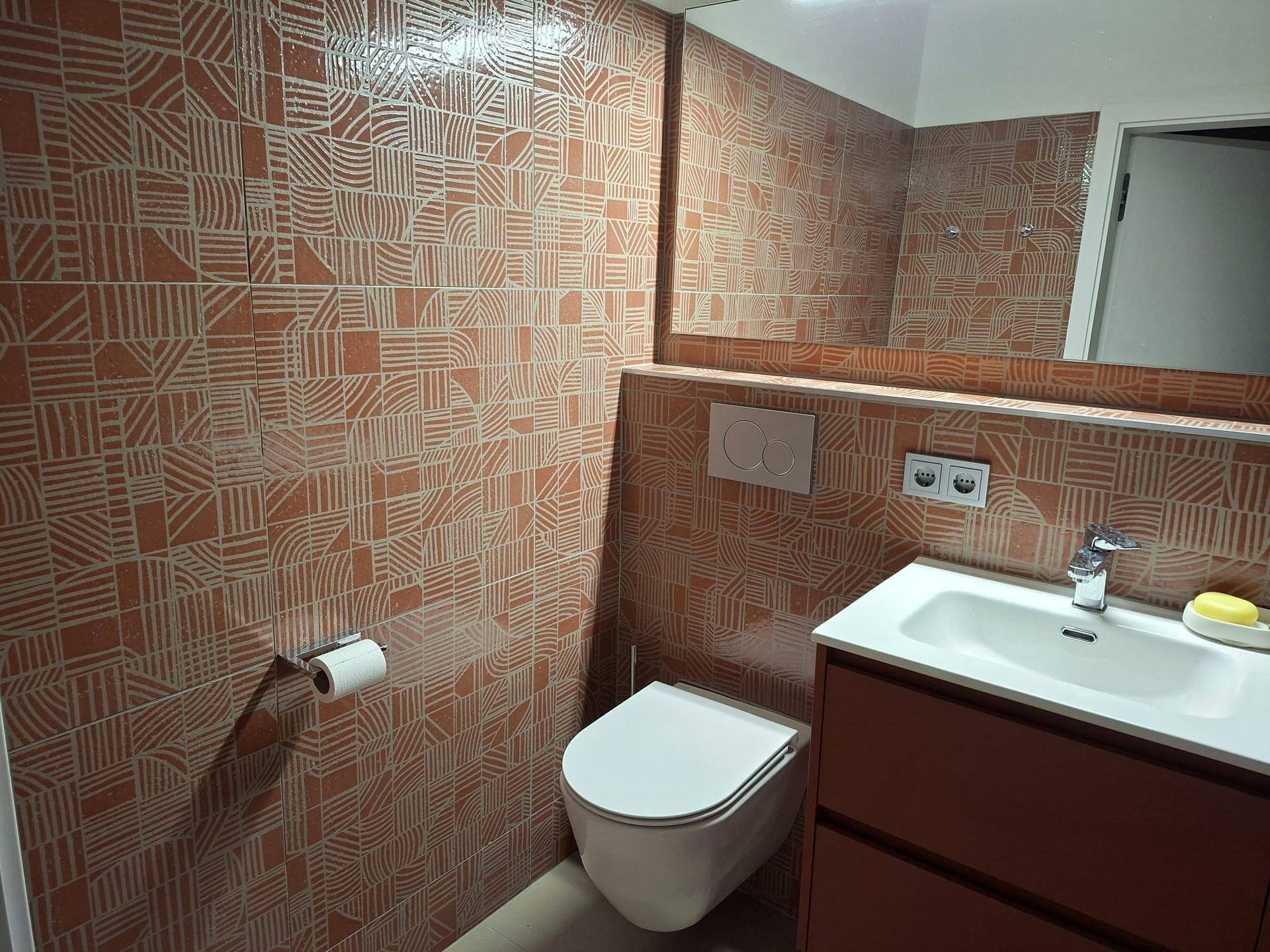 Badezimmer mit Dusche, wandhängendem WC und gemusterten Fliesen in warmen Erdtönen.