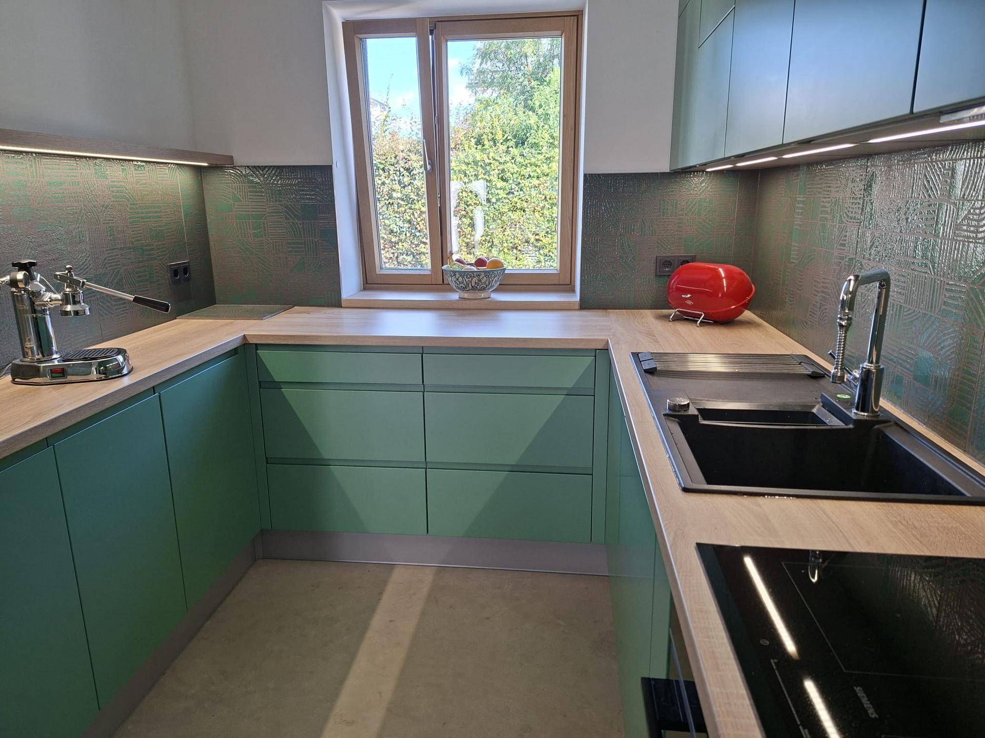 Moderne Küche mit mintgrünen Fronten, Holzarbeitsplatte und Fenster mit Blick ins Grüne.