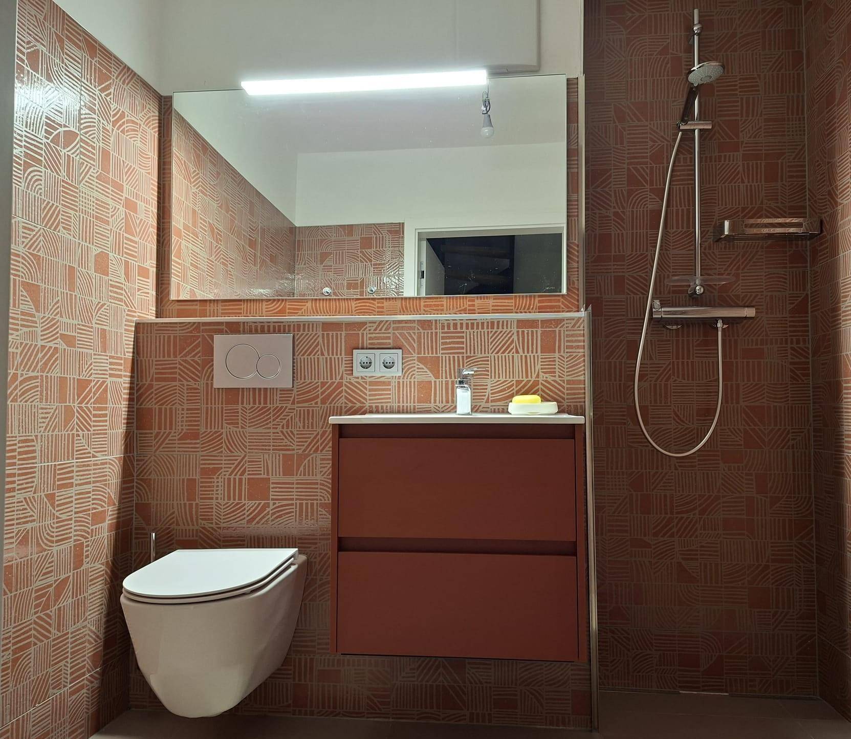 Modernes Badezimmer mit Dusche, Waschtisch und terracottafarbenen Fliesen mit Muster.