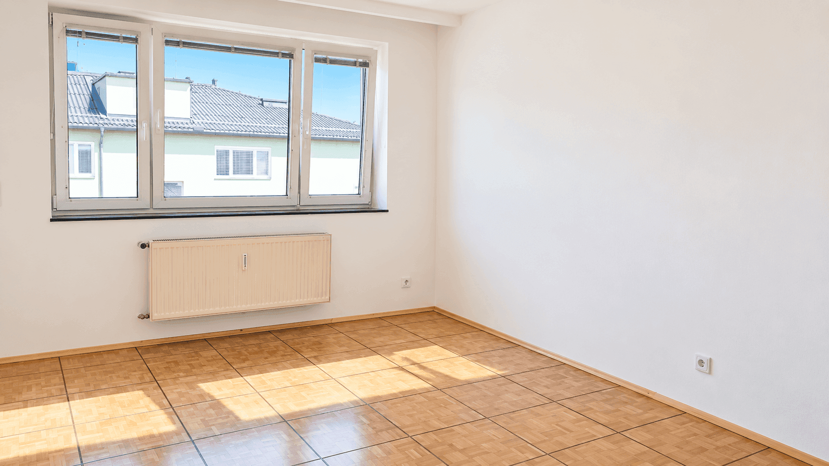 Helles Zimmer mit Parkettboden und einem großen Fenster, das viel Tageslicht hereinlässt.