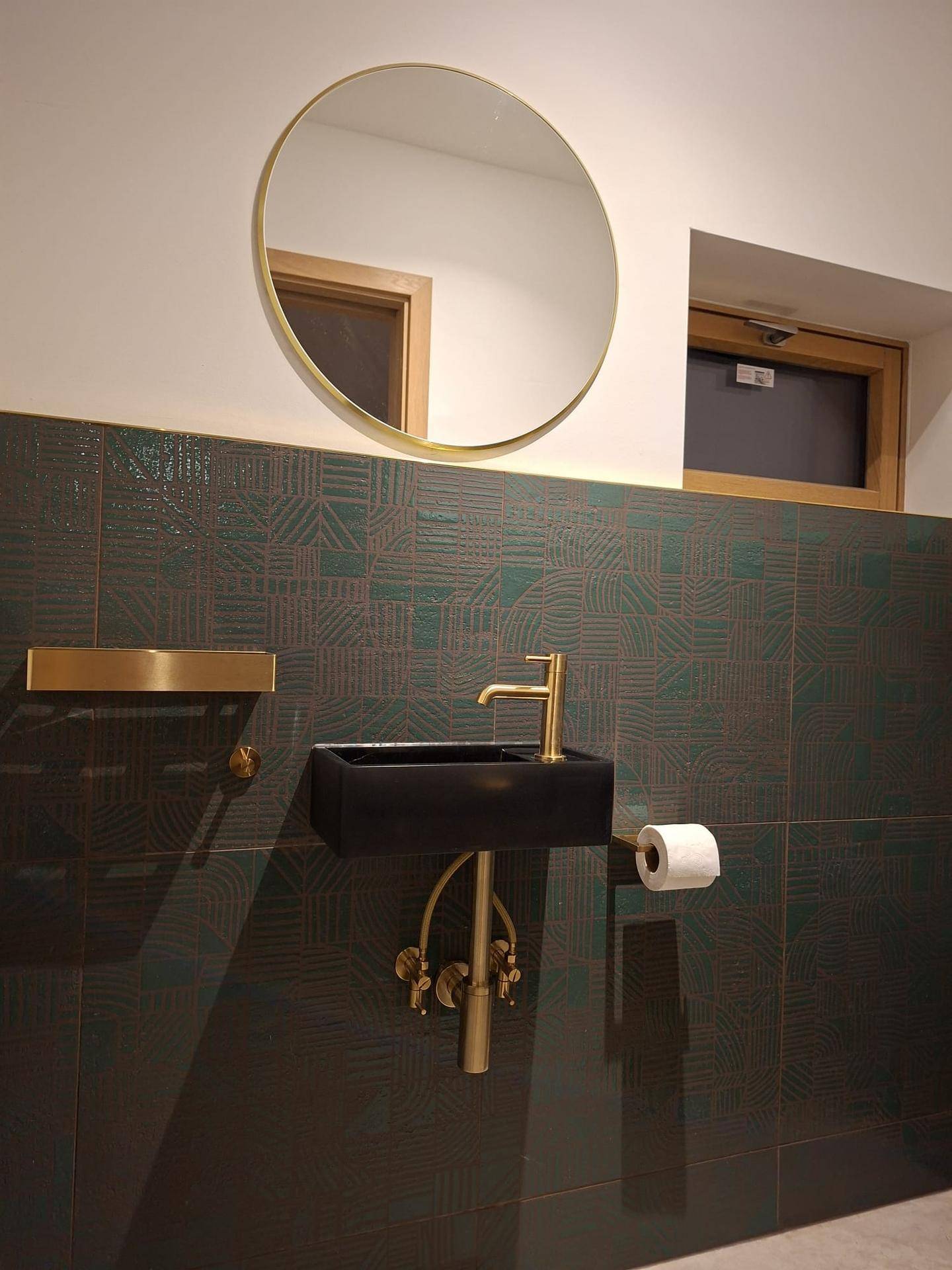 Stilvolles Gäste-WC mit kleinem Waschbecken, rundem Spiegel und goldenen Armaturen.