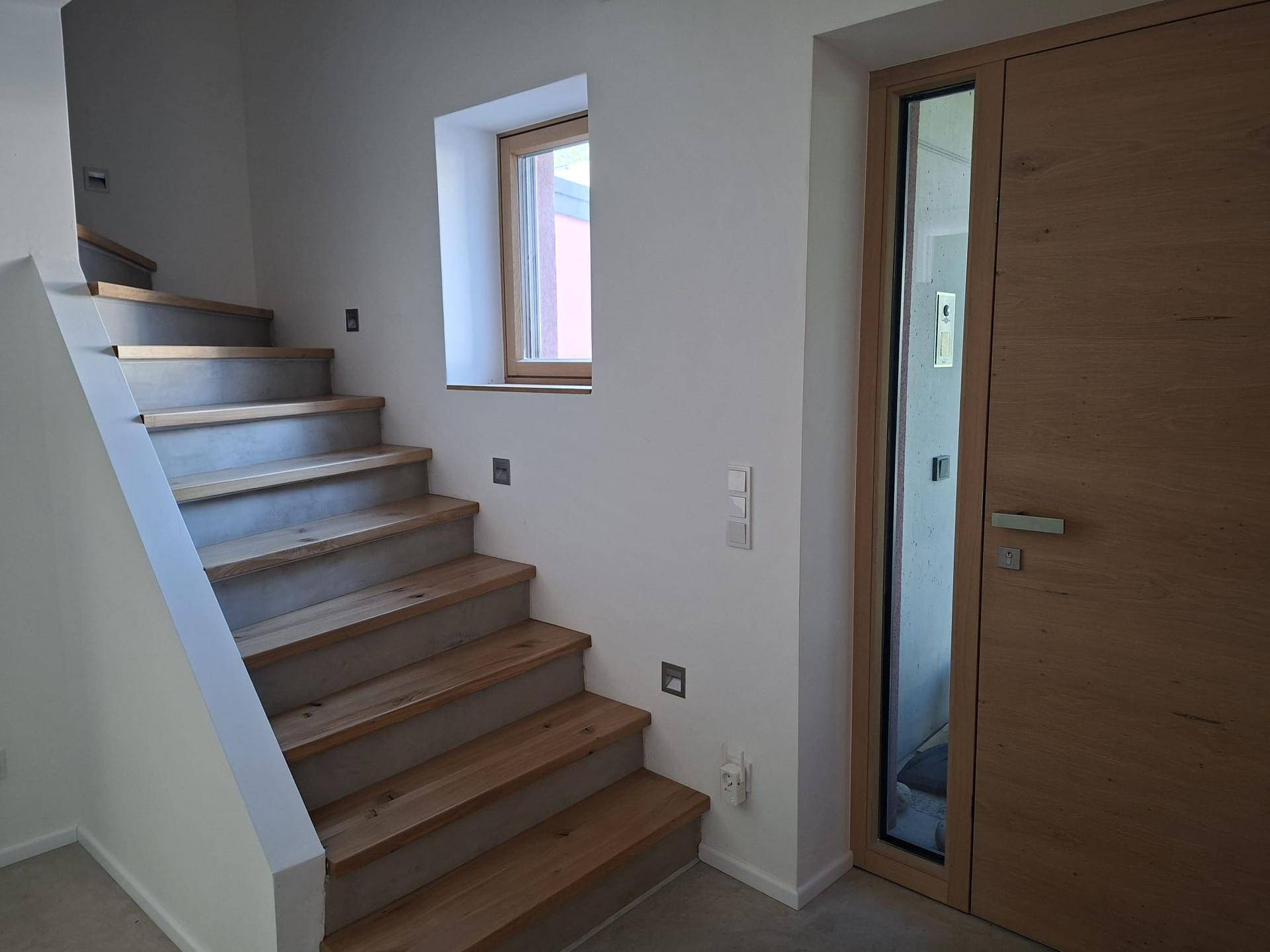 Heller Eingangsbereich mit Holztreppe, weiß gestrichenen Wänden und Holztür.