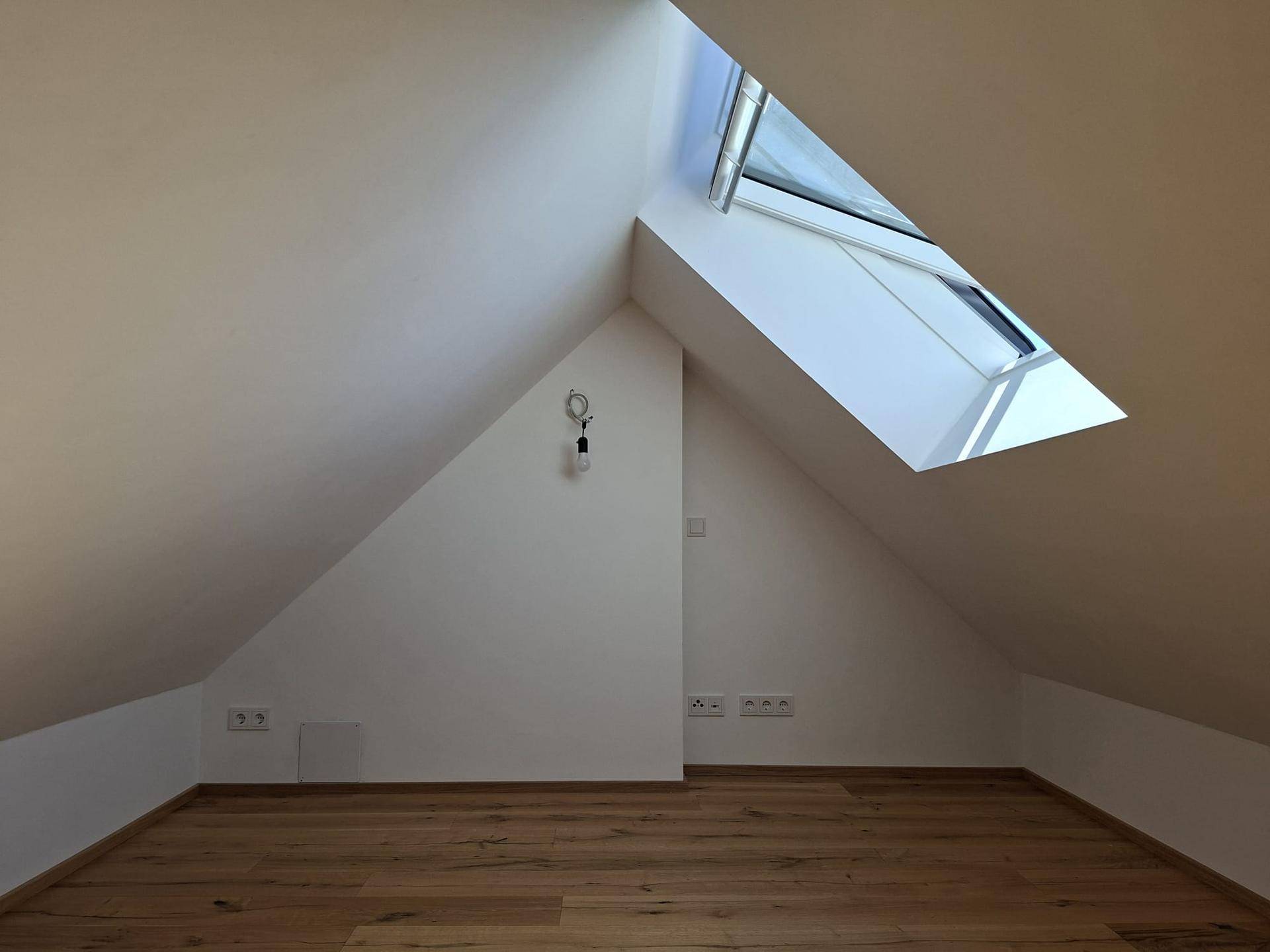 Geräumiger Dachboden mit Holzboden, schrägen Wänden und einem hellen Dachfenster.