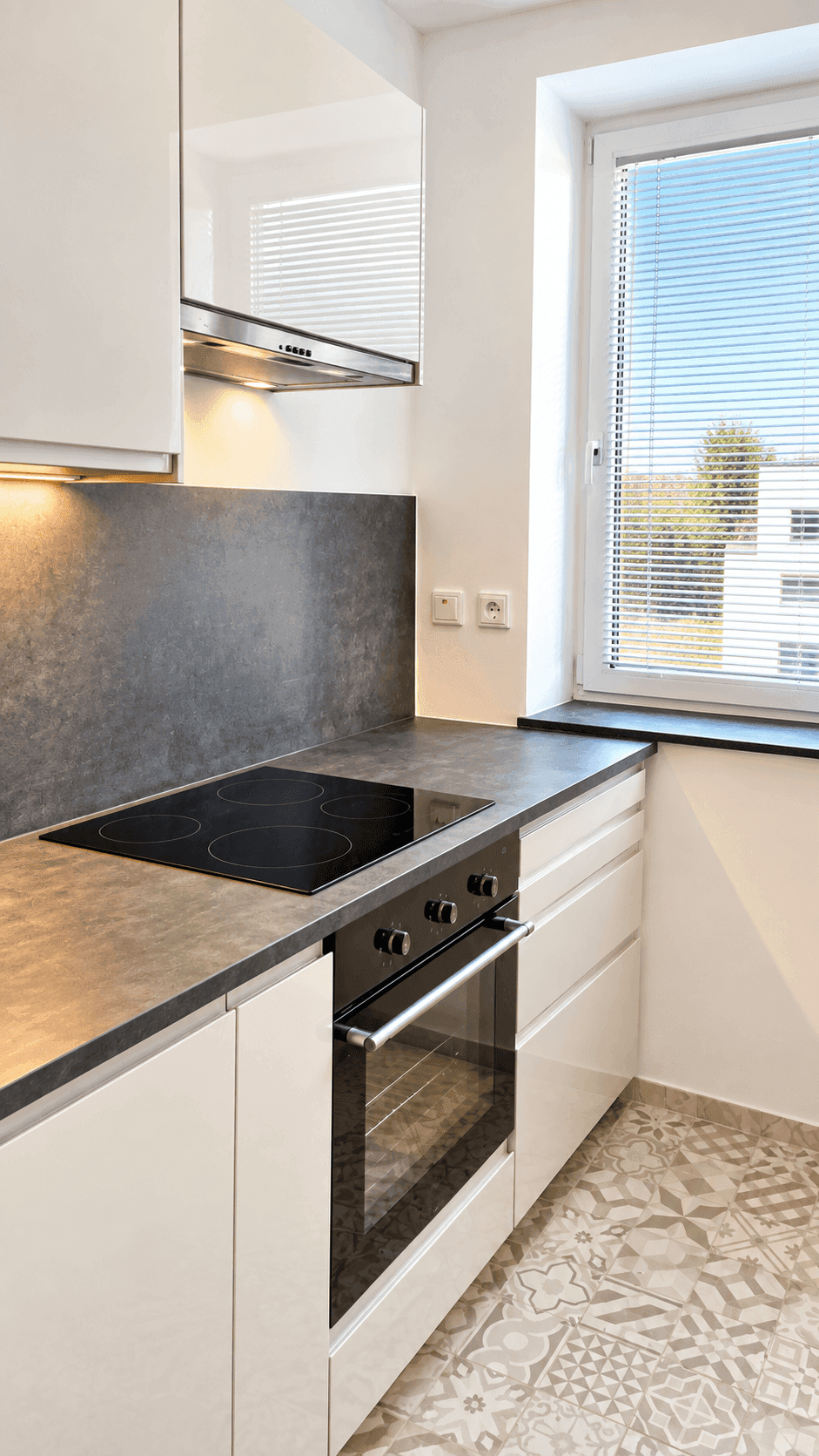 Helle, moderne Küche mit Induktionskochfeld, Backofen und Fenster mit Jalousien.