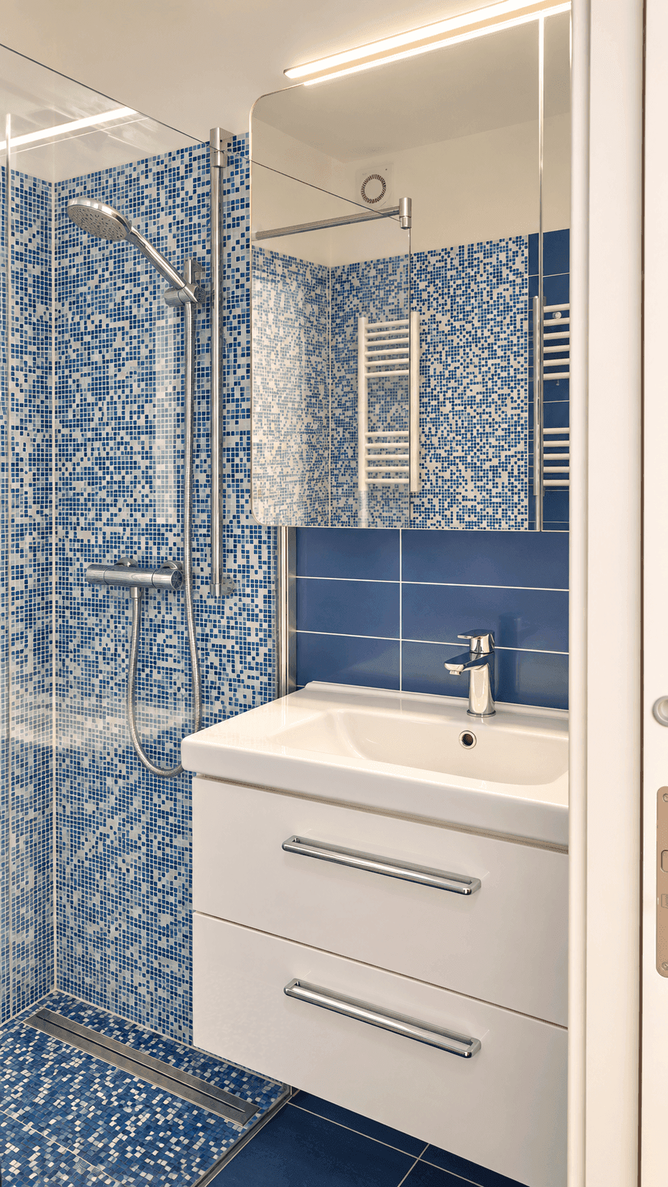Modernes Badezimmer mit blauen Mosaikfliesen, Dusche und Waschtisch mit Spiegelschrank.