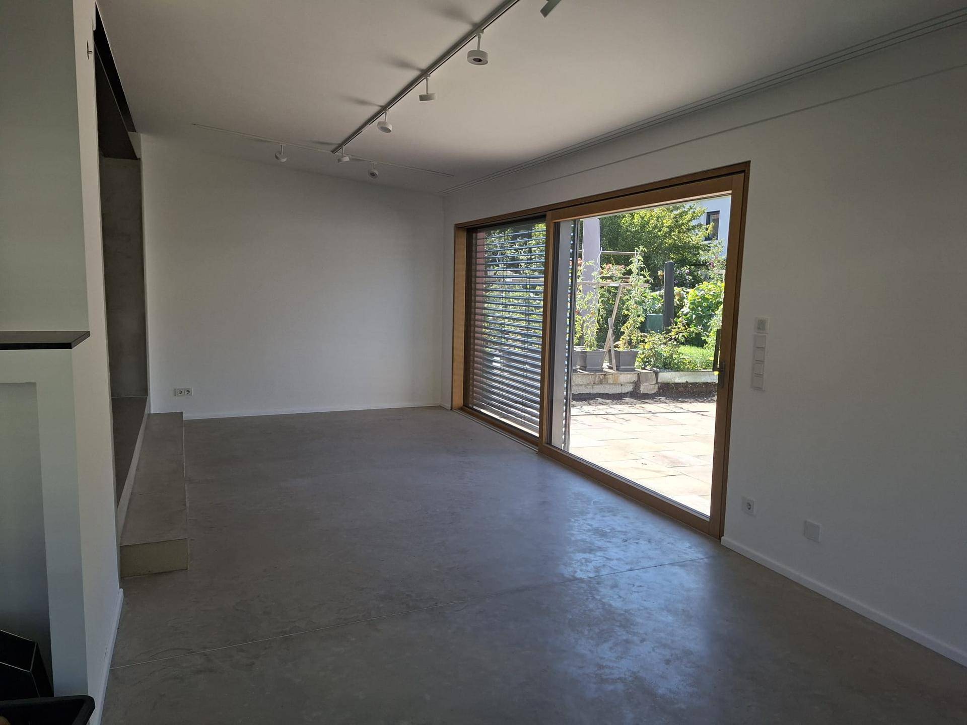 Helles Wohnzimmer mit Betonboden und breiter Schiebetür zum Gartenbereich.
