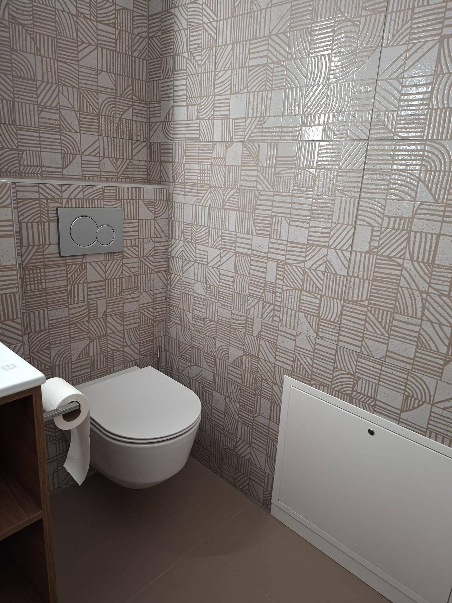 Badezimmer mit wandhängendem WC, gemusterten Fliesen und integriertem Spülkasten.