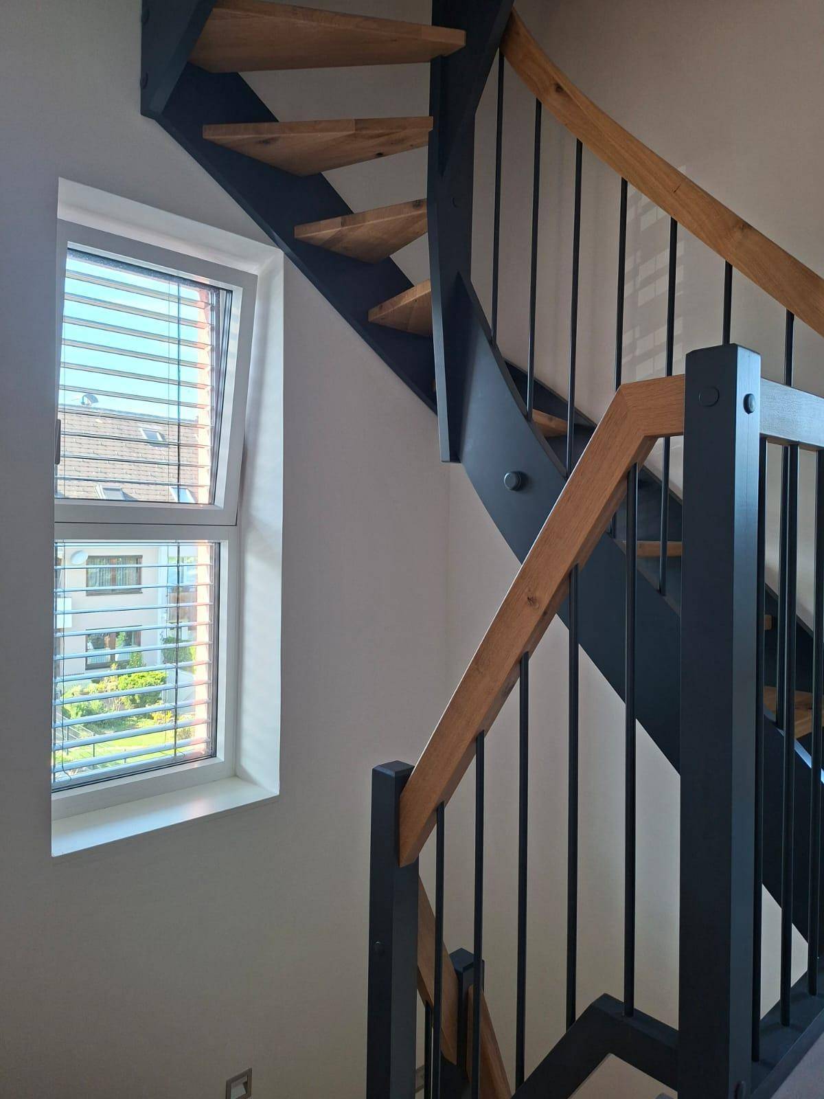 Treppenhaus mit Holzstufen, schwarzem Geländer und einem Fenster für natürliches Licht.