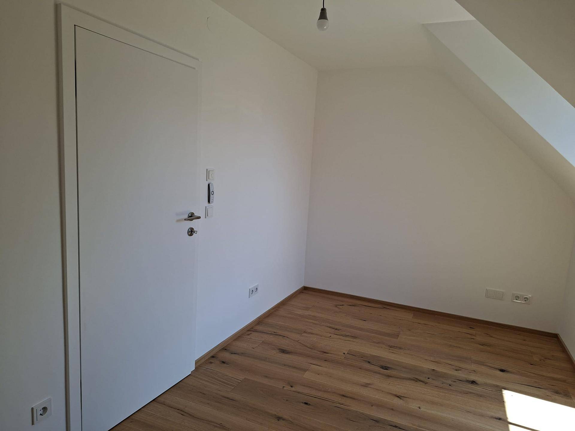 Dachzimmer mit Holzboden, weißen Wänden und einer modernen Tür.