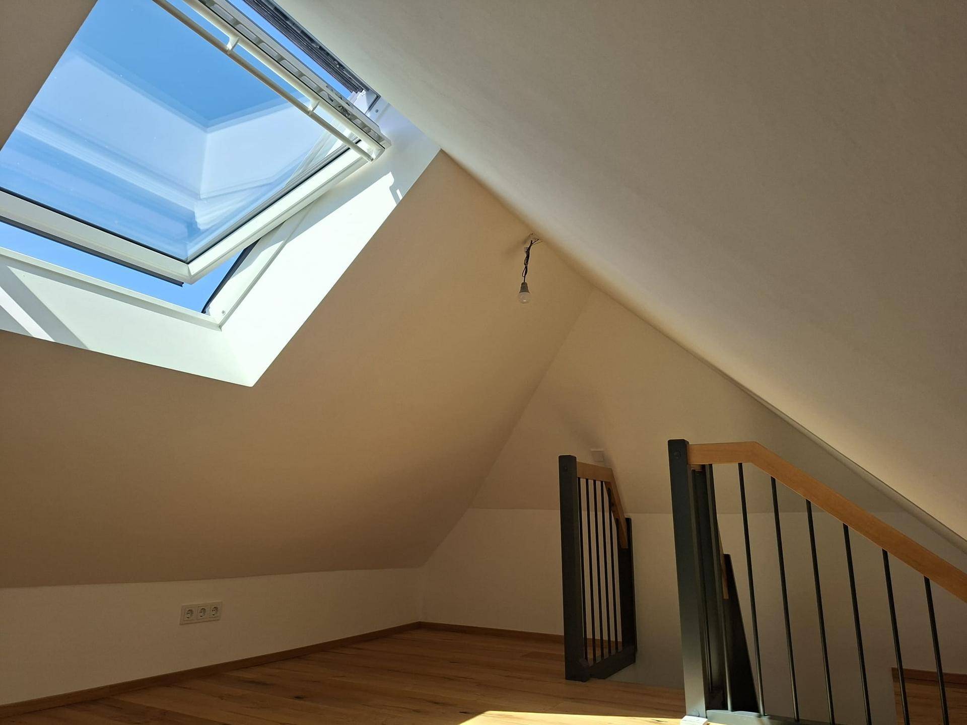 Heller Dachbodenbereich mit Holzboden, schrägen Wänden und großem Dachfenster.