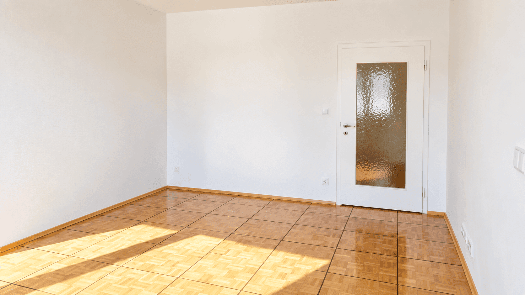 Leeres, helles Zimmer mit Parkettboden und einer Tür mit Glaseinsatz, ideal für individuelle Gestaltung.