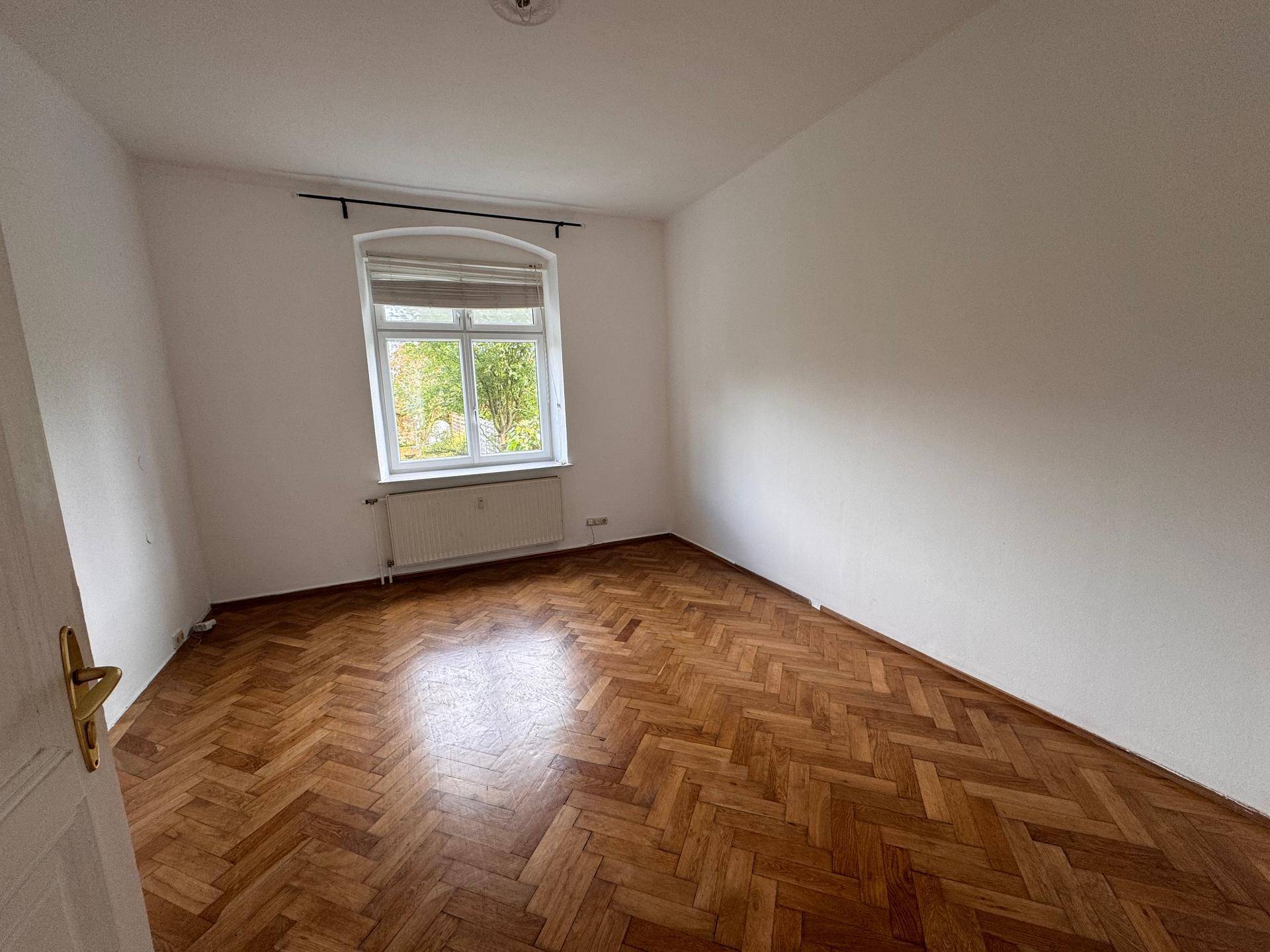 Ruhiges Zimmer mit Fischgrätparkett und Fenster mit Blick ins Grüne, geeignet als Schlafzimmer.
