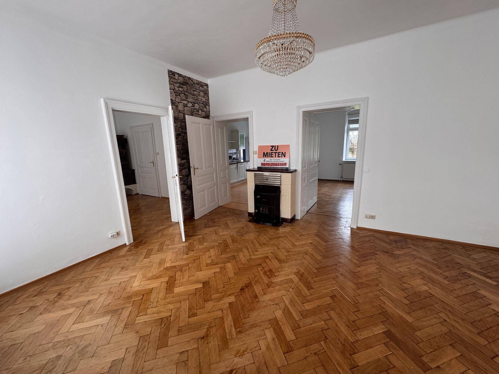 Großes Wohnzimmer mit Fischgrätparkett, Kaminofen und Zugang zu mehreren Räumen.