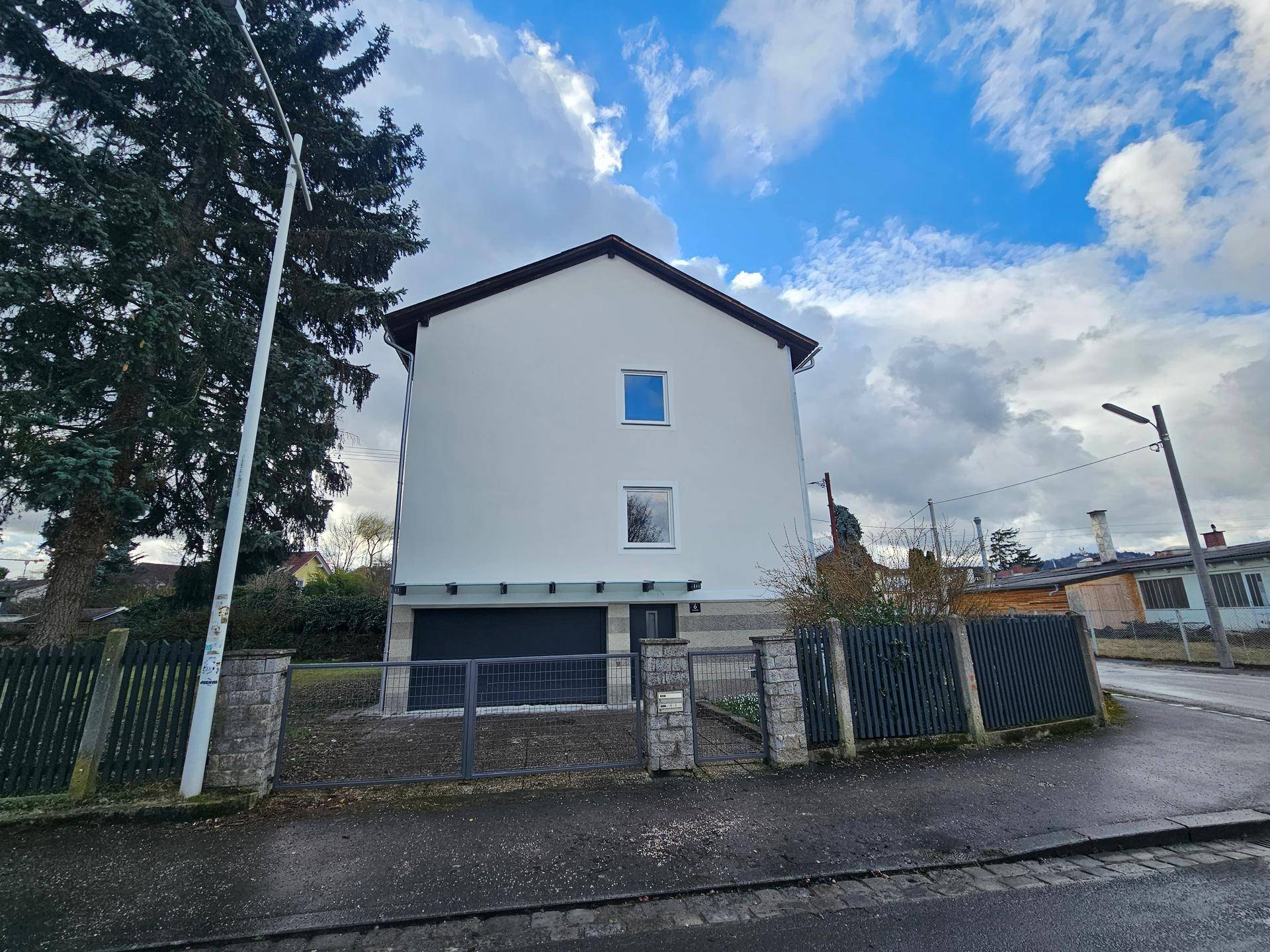 Vorderansicht des Hauses mit integrierter Garage, modernem Zaun und Zufahrt von der Straße.