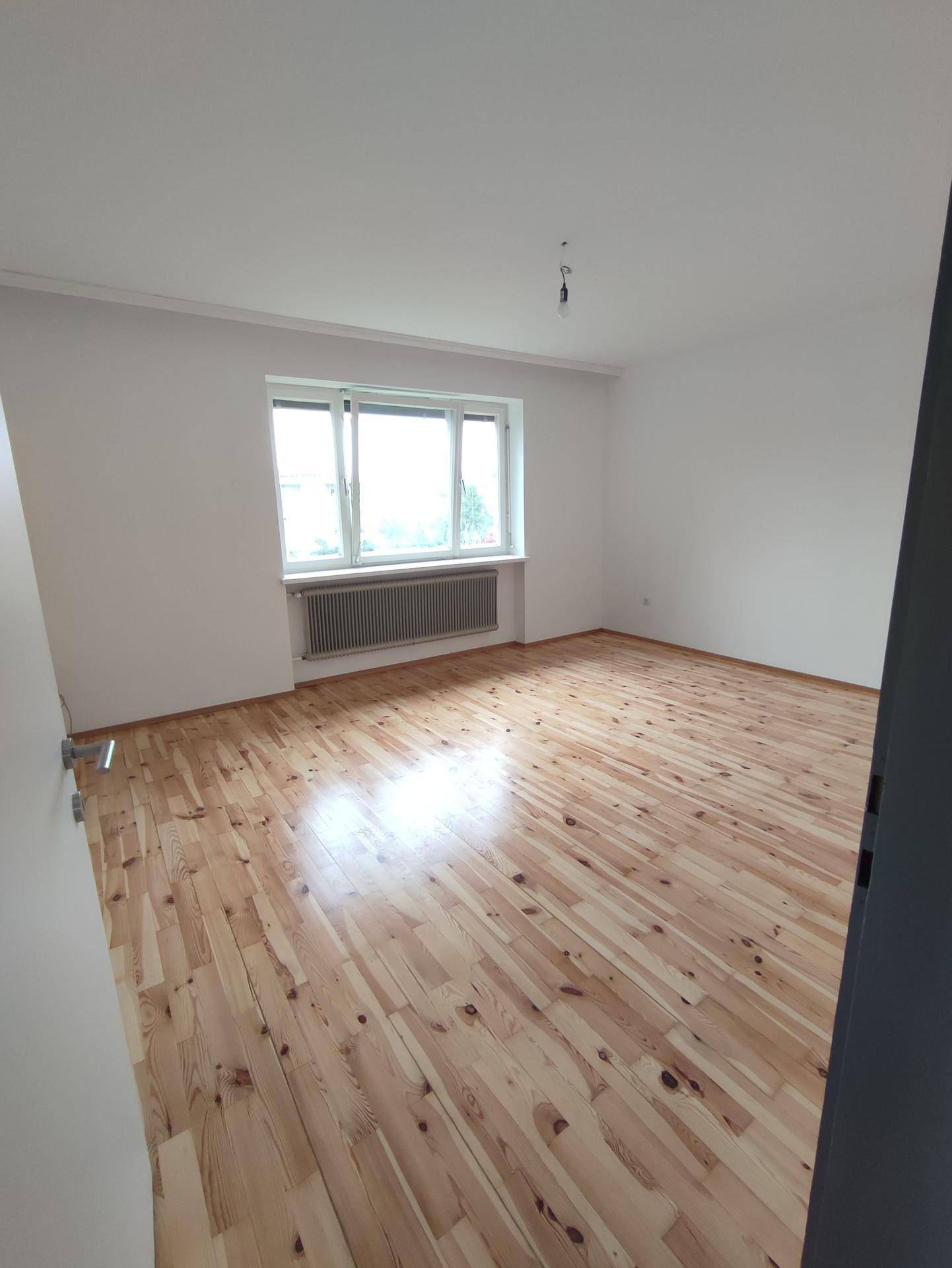 Lichtdurchflutetes Zimmer mit Holzdielenboden und breitem Fenster für viel Helligkeit.