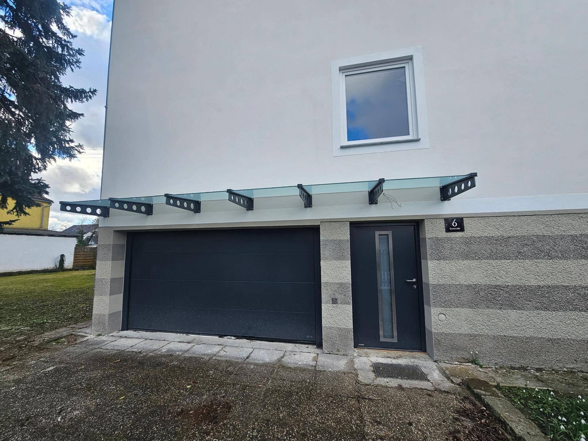Detailansicht der Garage und des Hauseingangs mit einer modernen Glasüberdachung.