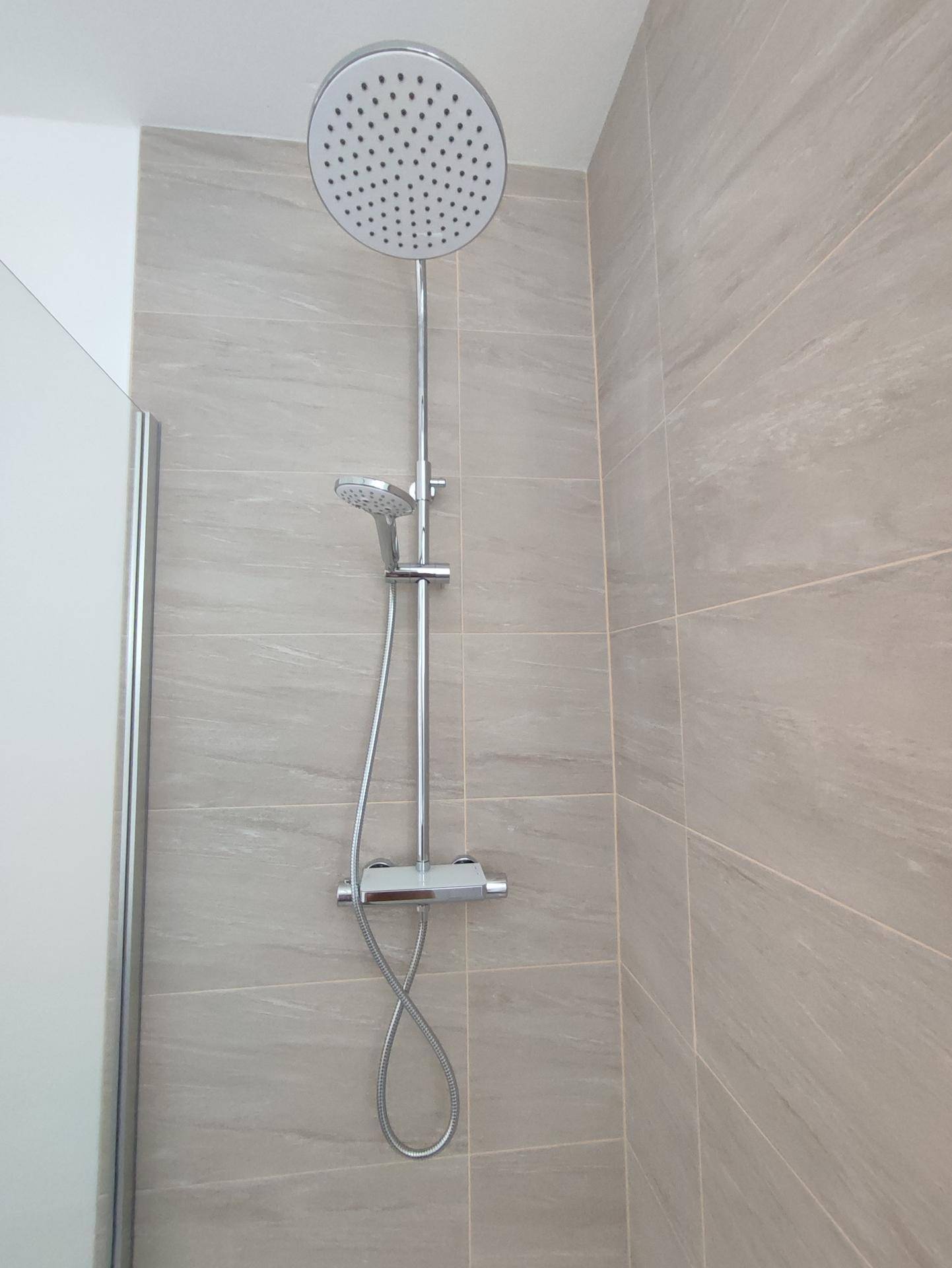 Moderne Regendusche mit zusätzlicher Handbrause und hellen Wandfliesen im Badezimmer.