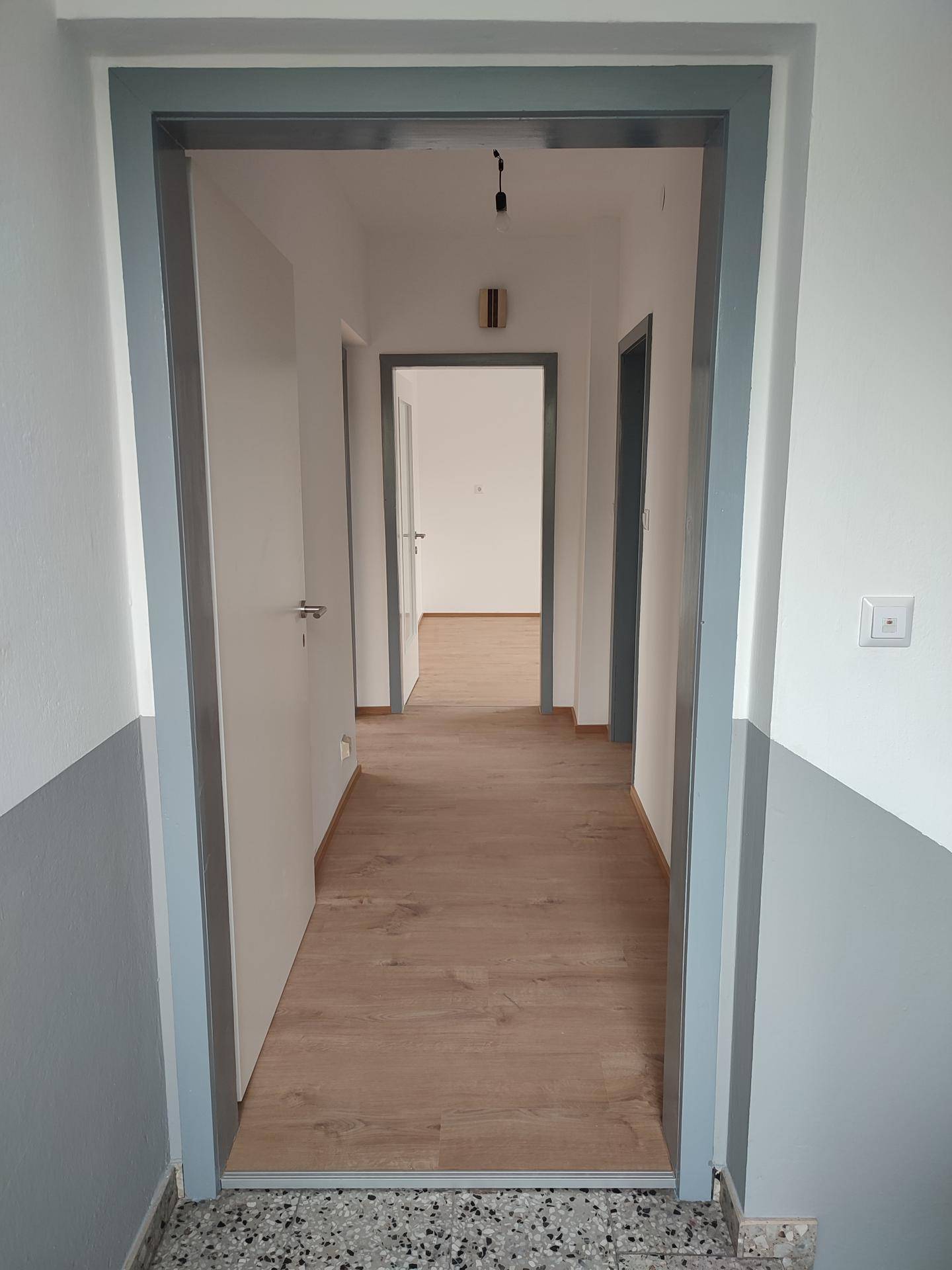 Heller Flur mit modernem Laminatboden und frisch gestrichenen Wänden in Weiß und Grau.